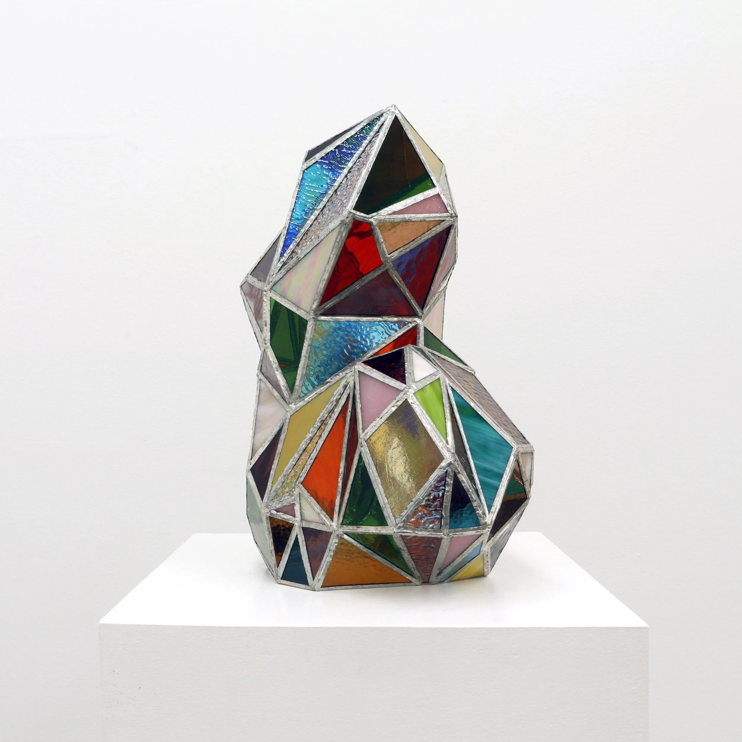 A stained glass sculpture with geometric shapes, set on a white surface against a white background.