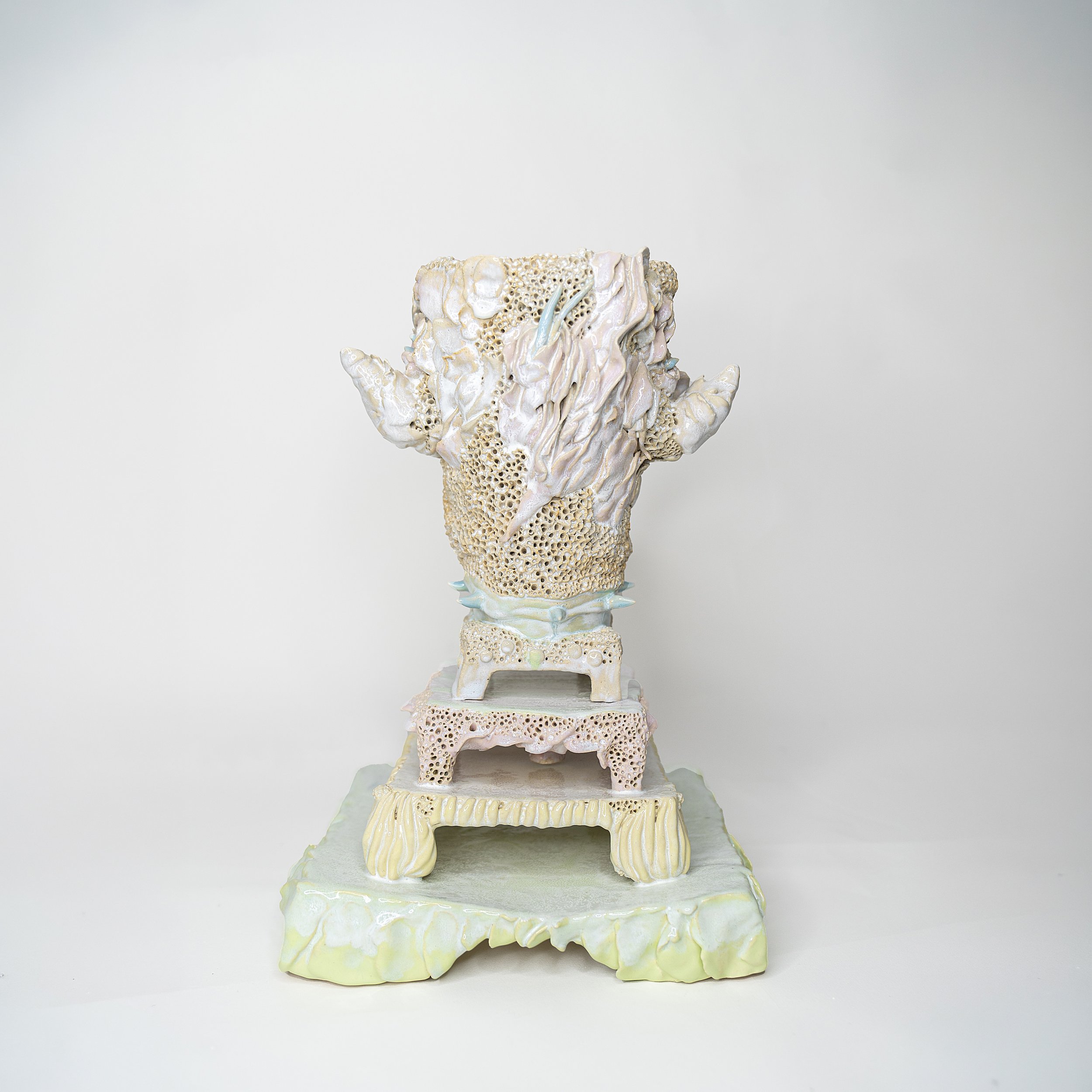 A multi-tiered ceramic sculpture with textured, organic shapes resembling coral or geological formations, in pastel shades of white, cream, light pink, and pale green.