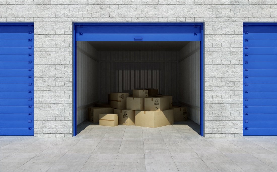 Open storage unit with cardboard boxes inside, featuring blue door and brick wall exterior.
