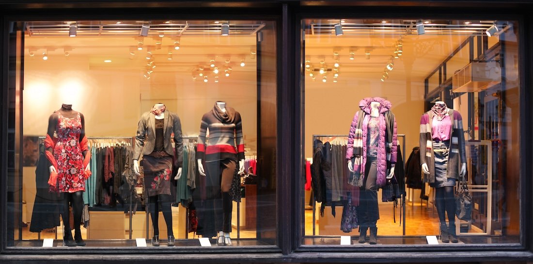 Storefront with mannequins displaying women's winter clothing, including dresses, coats, and sweaters.