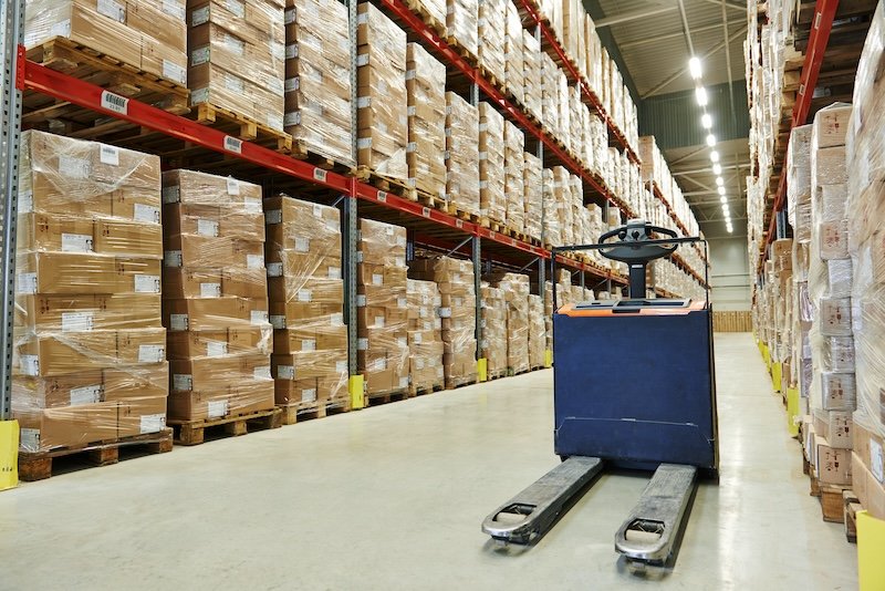 Warehouse with shelves stacked with boxes and a pallet jack on the floor.