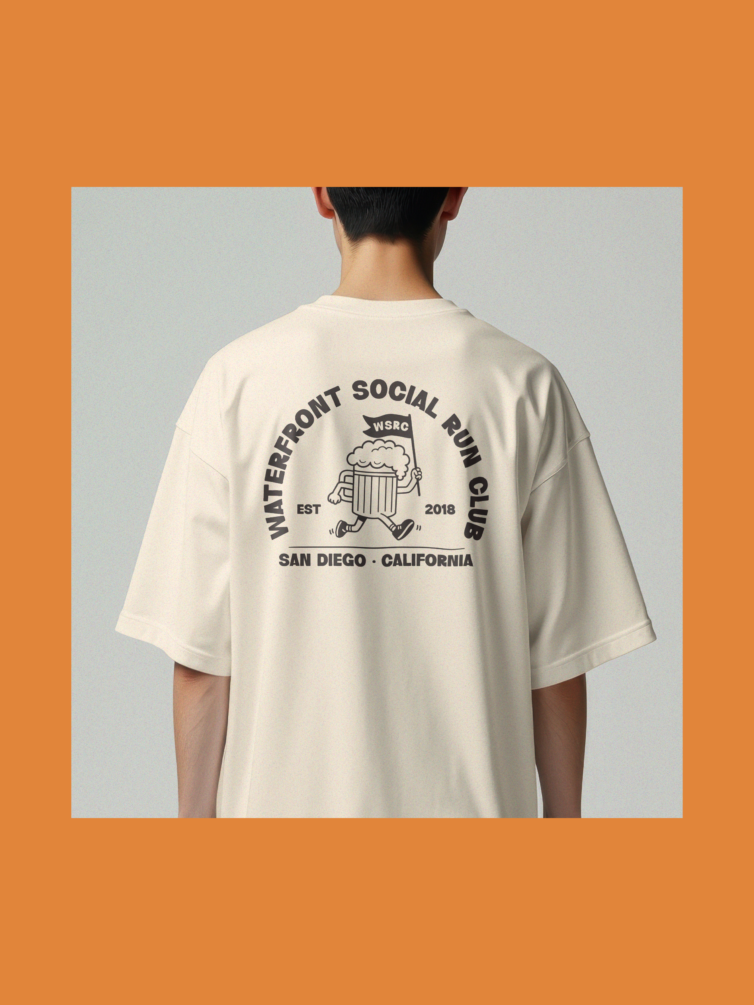 Back view of a person wearing a beige t-shirt with a black graphic design and text that reads 'Waterfront Social Run Club' and 'San Diego California'. The person has short dark hair and fair skin. The background is plain.