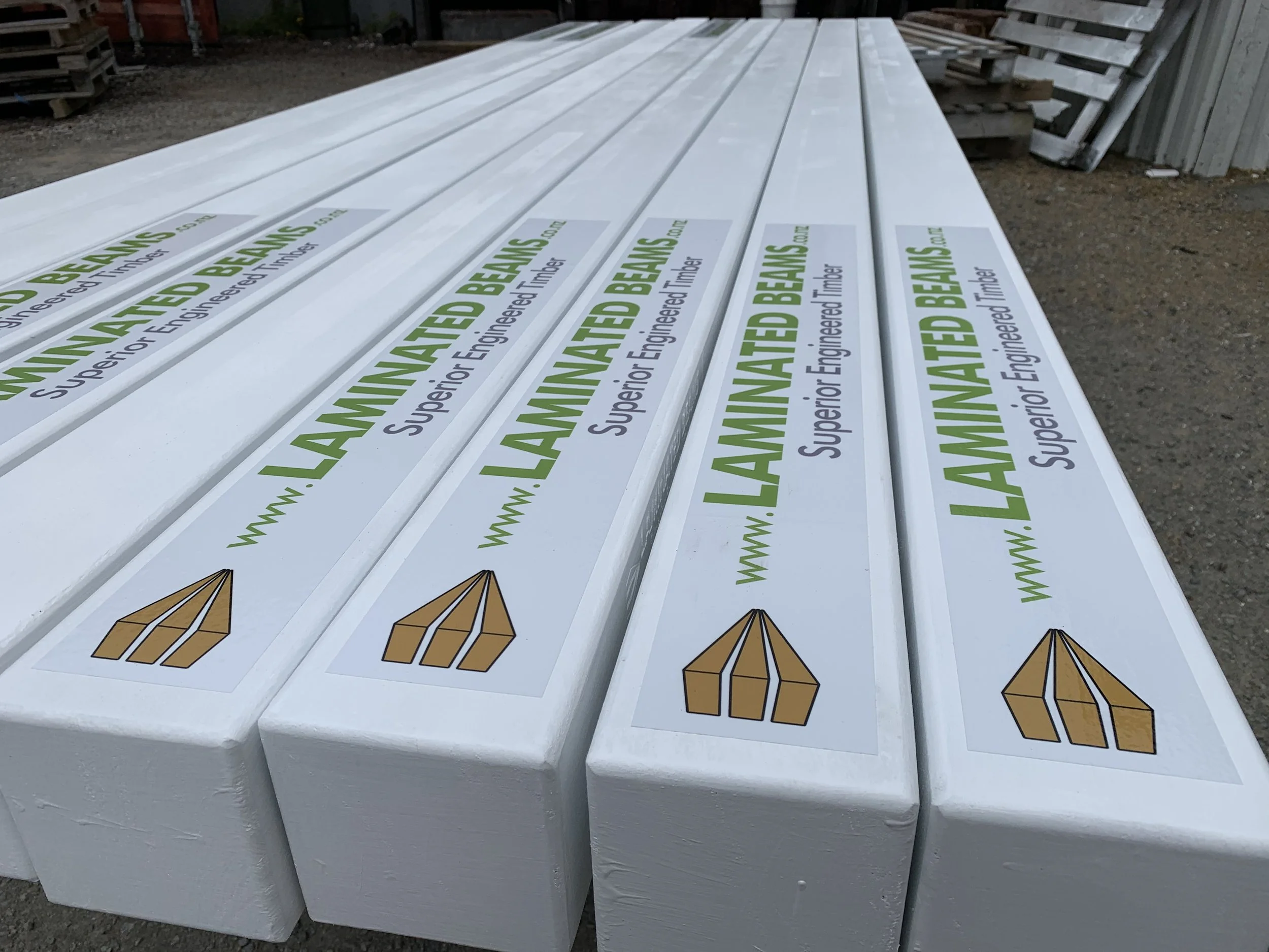 Stacked white lumber boards with a printed warning label about engineered timber at an construction site.