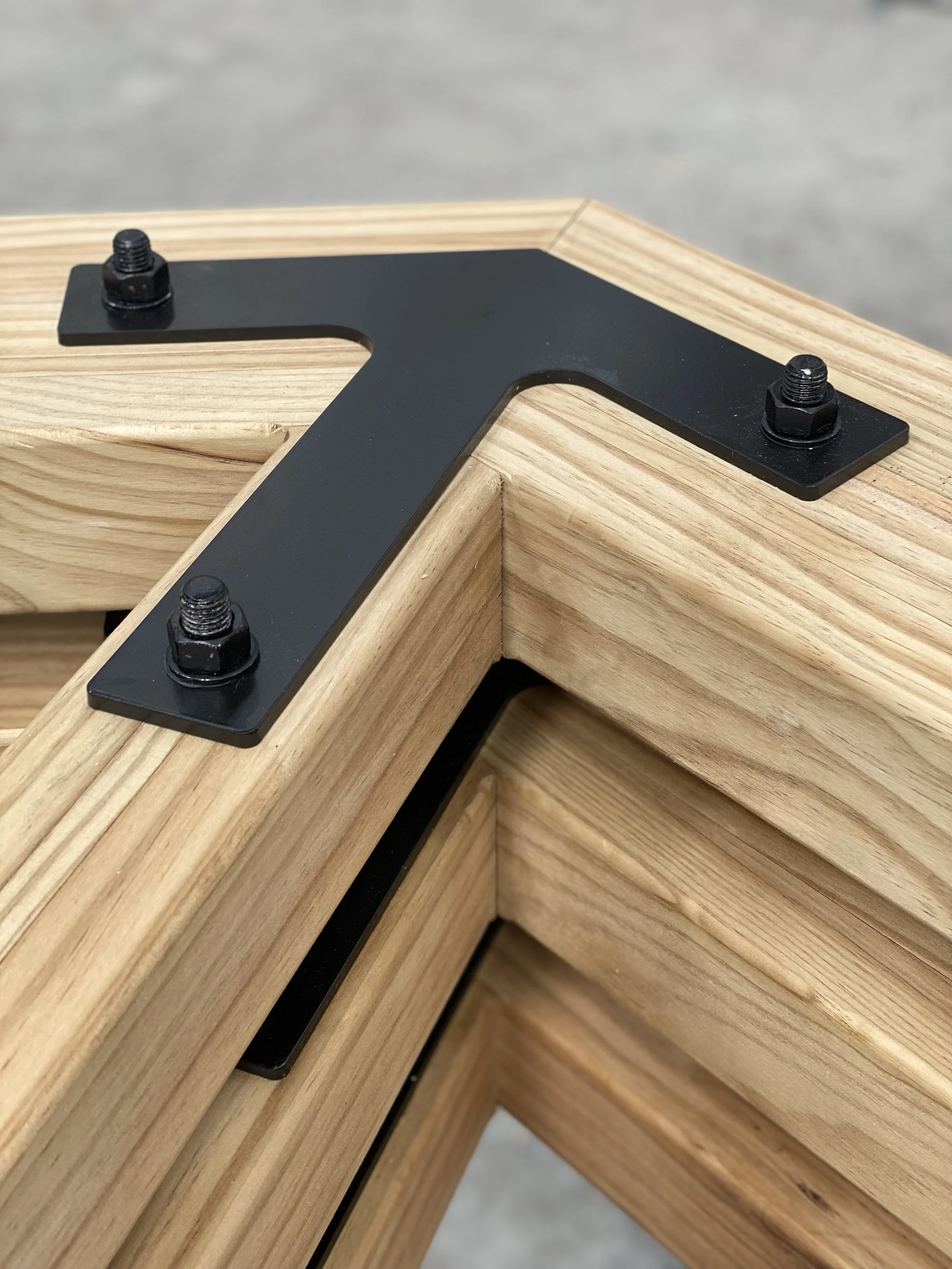 Black metal bracket with bolts attached to a wooden surface.