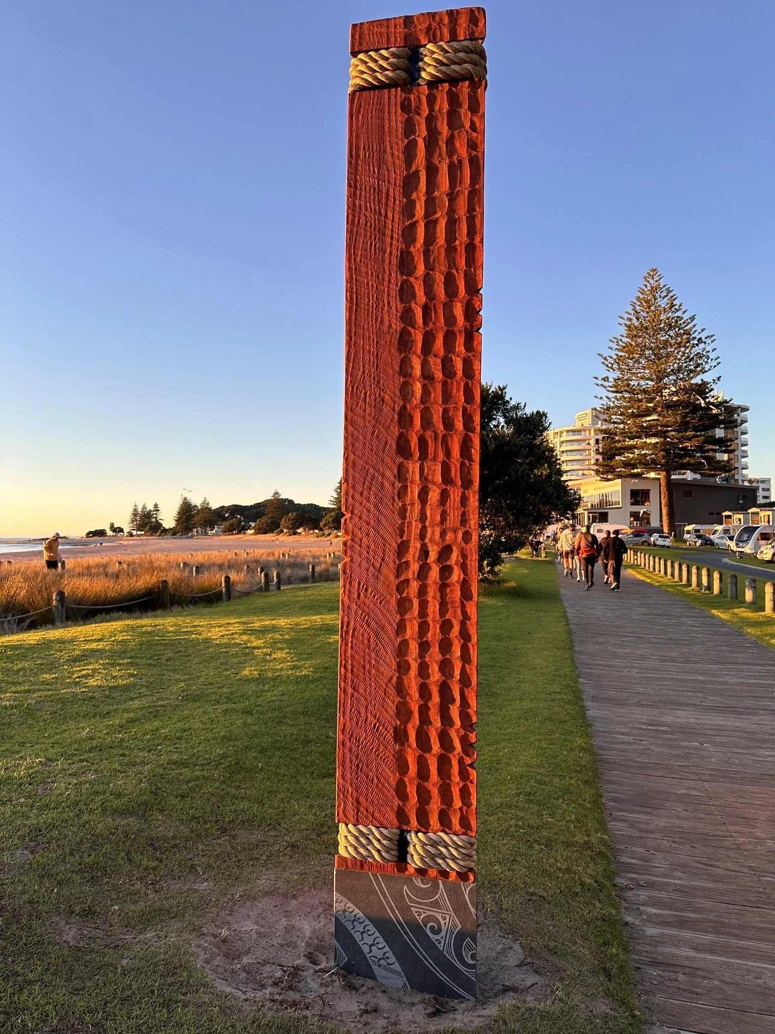 A tall glulam timber sculpture with intricate carvings and rope accents located at the Mauao.