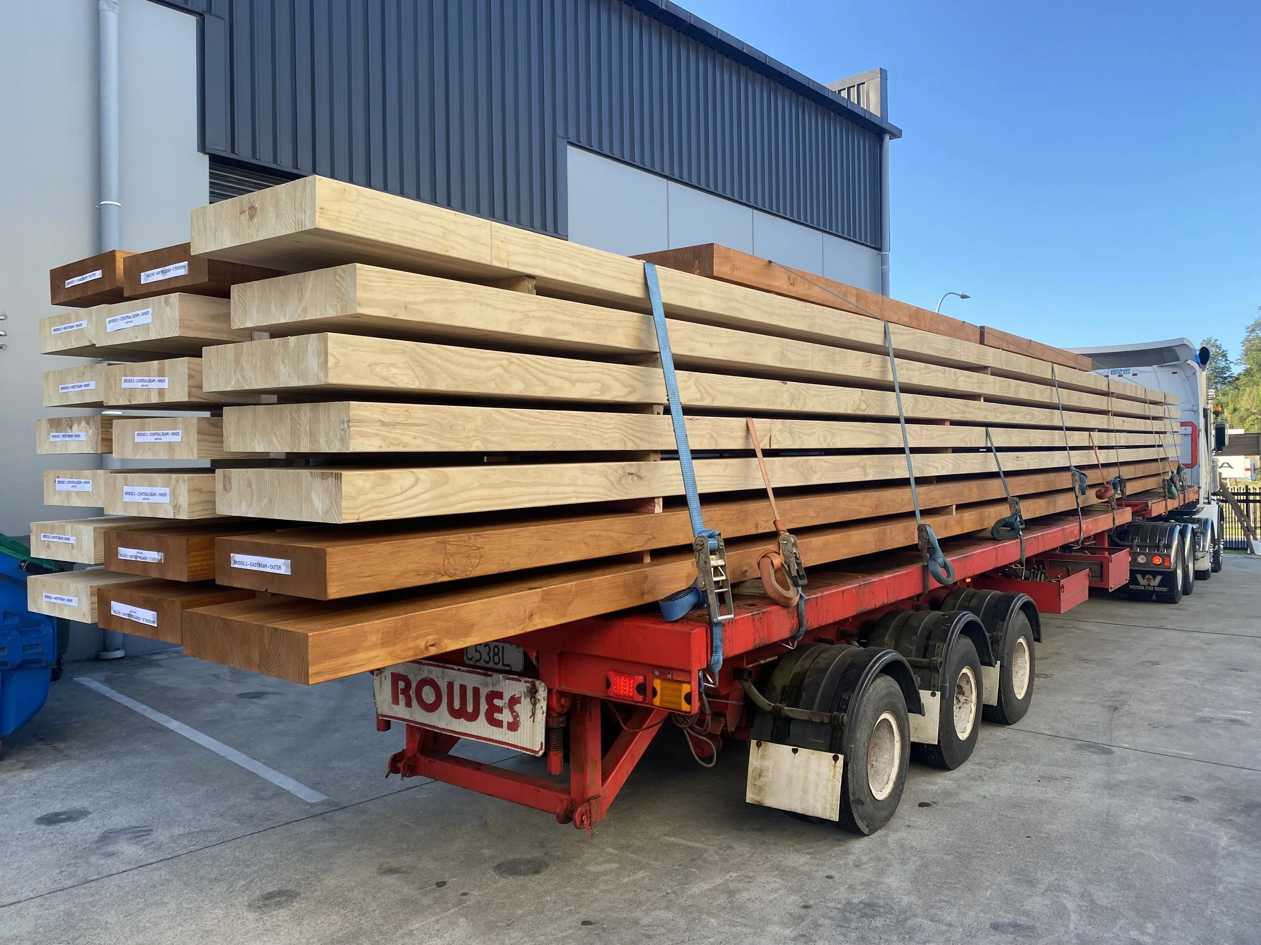 A flatbed truck carrying large glulam timber beams for delivery.