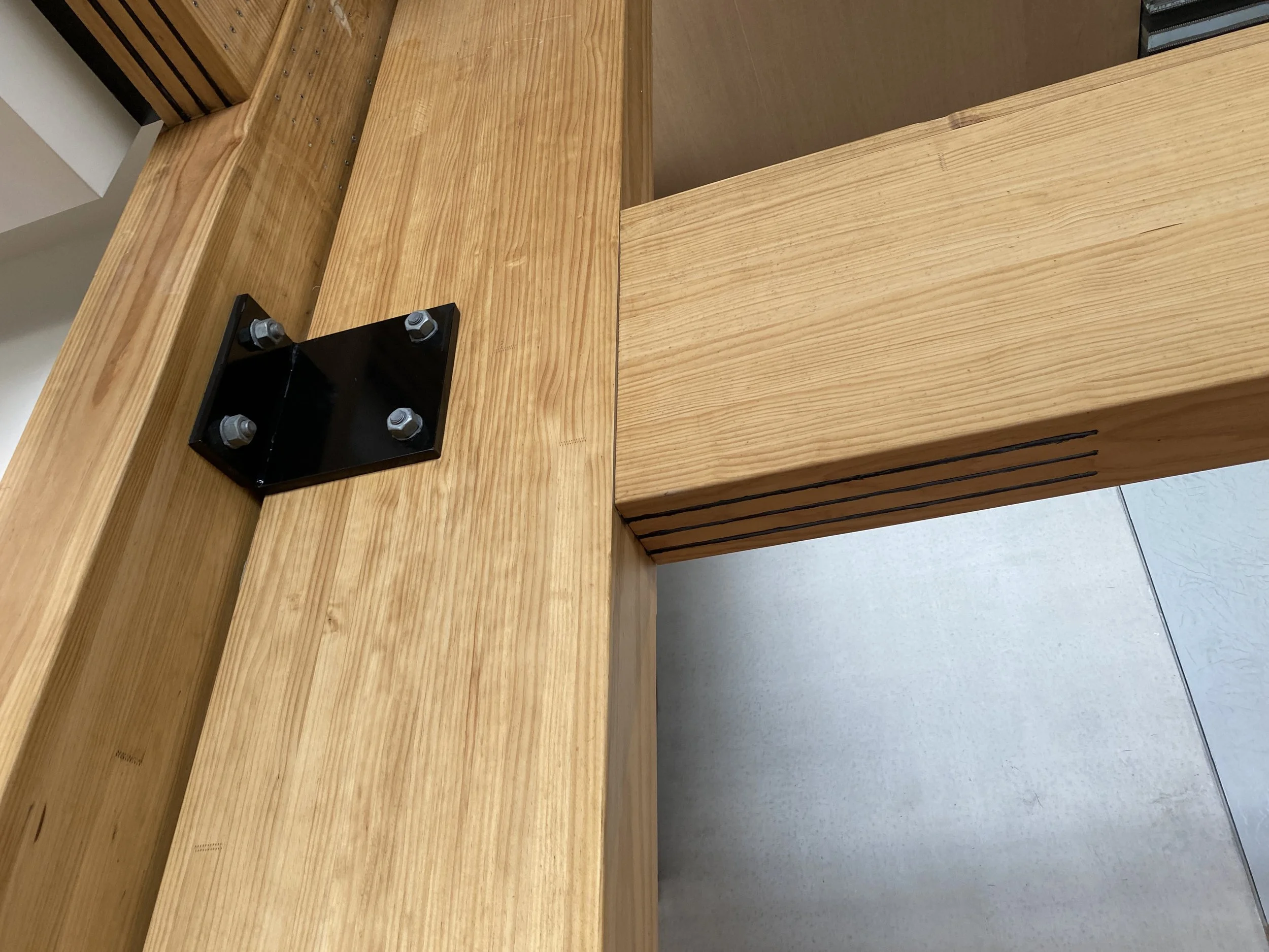 Close-up of a wooden structure with visible metal bolts and black brackets.