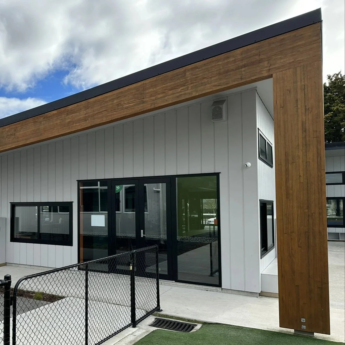 Modern building with white vertical siding, large glass doors, and a prominent glulam timber architectural element