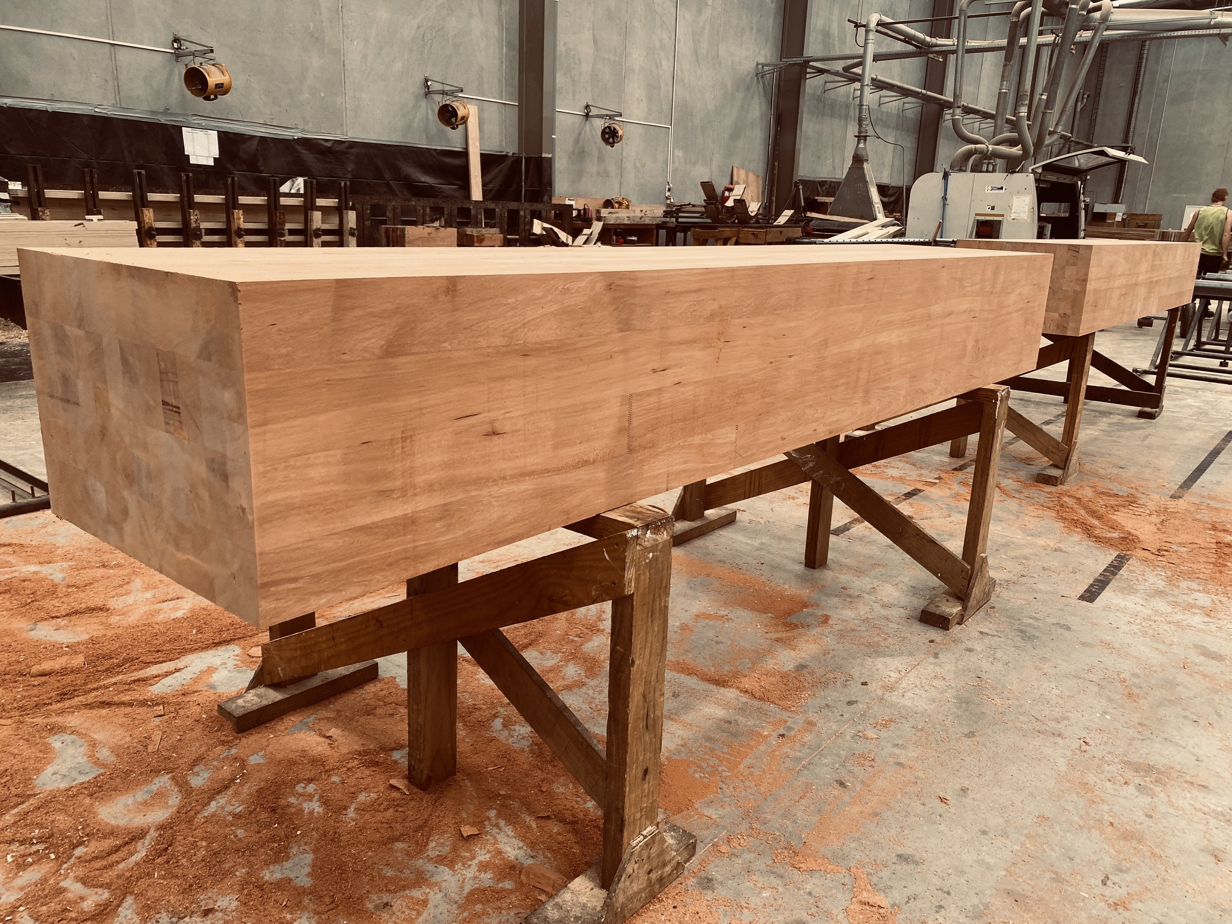 Large rectangular wooden block placed on sawhorses in a woodworking shop with machinery and tools in the background.