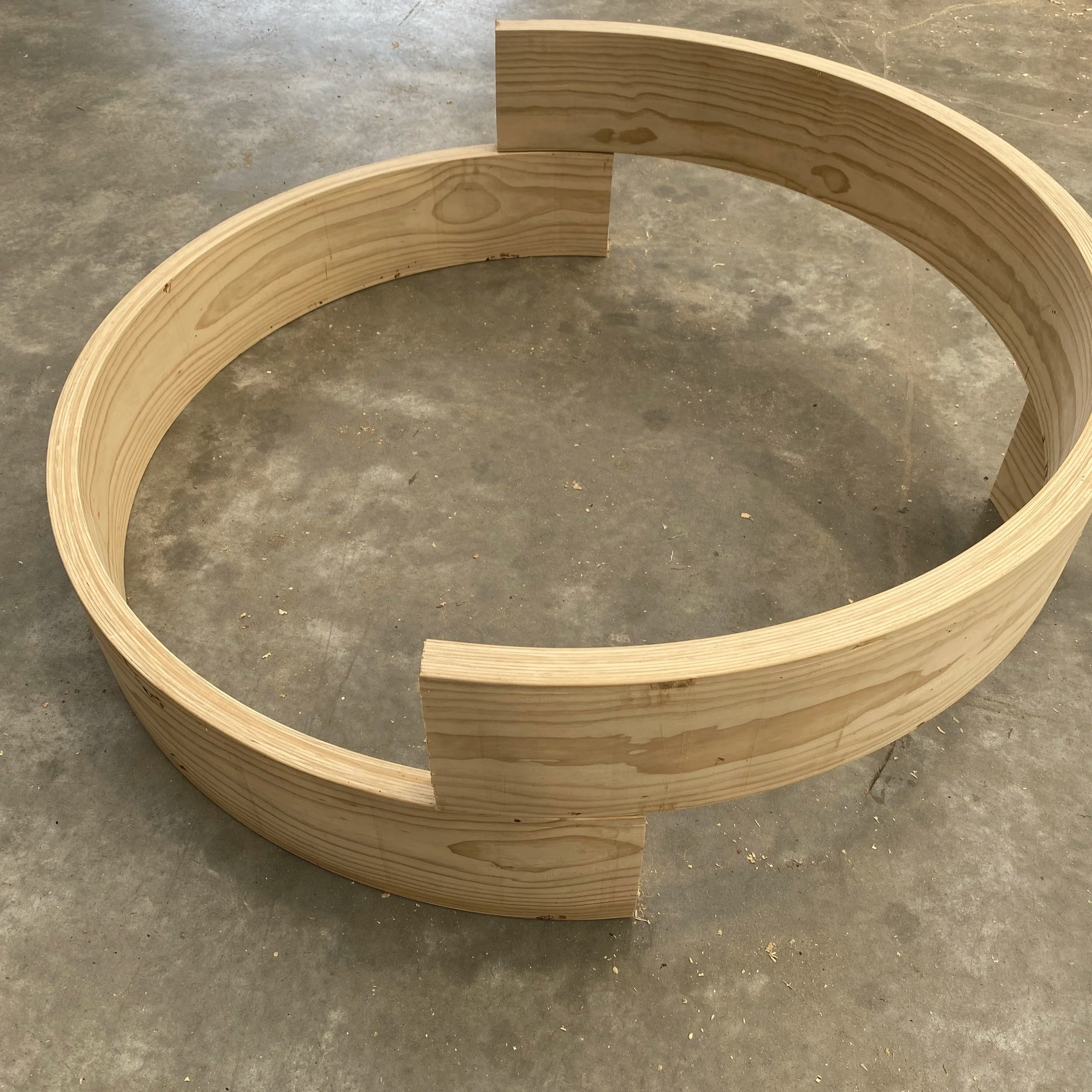 Curved wooden structure made of several thin layers of wood, placed on a concrete floor.