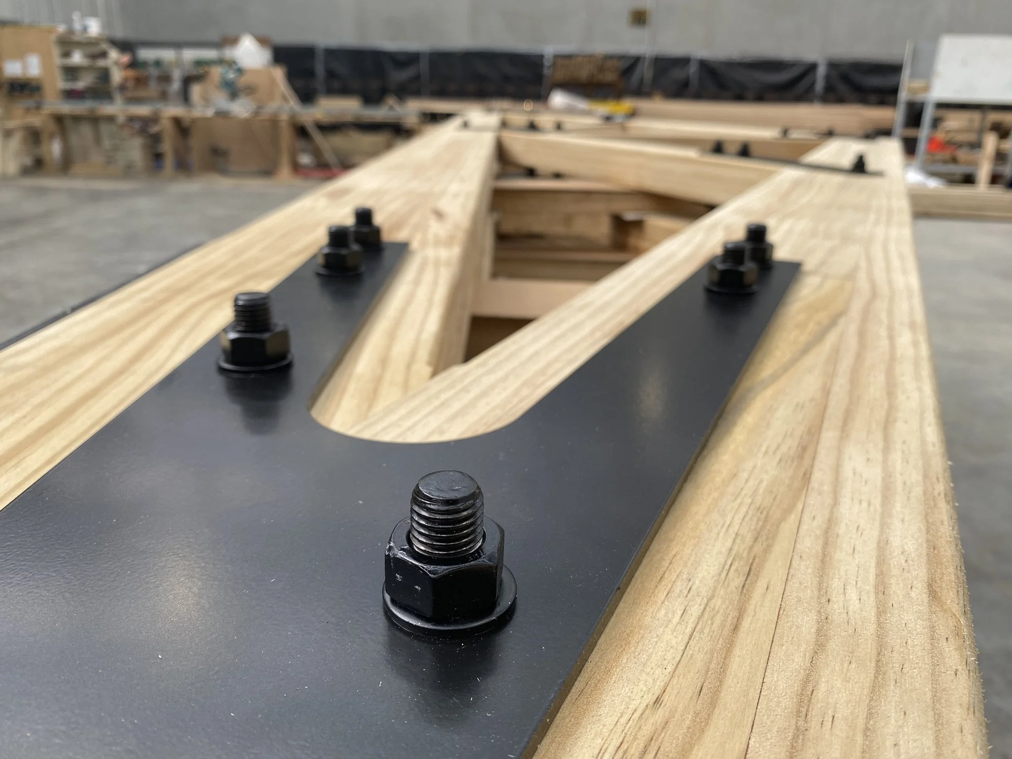 Close-up view of a woodworking project with screws and bolts on a black metal and wooden surface in a workshop.