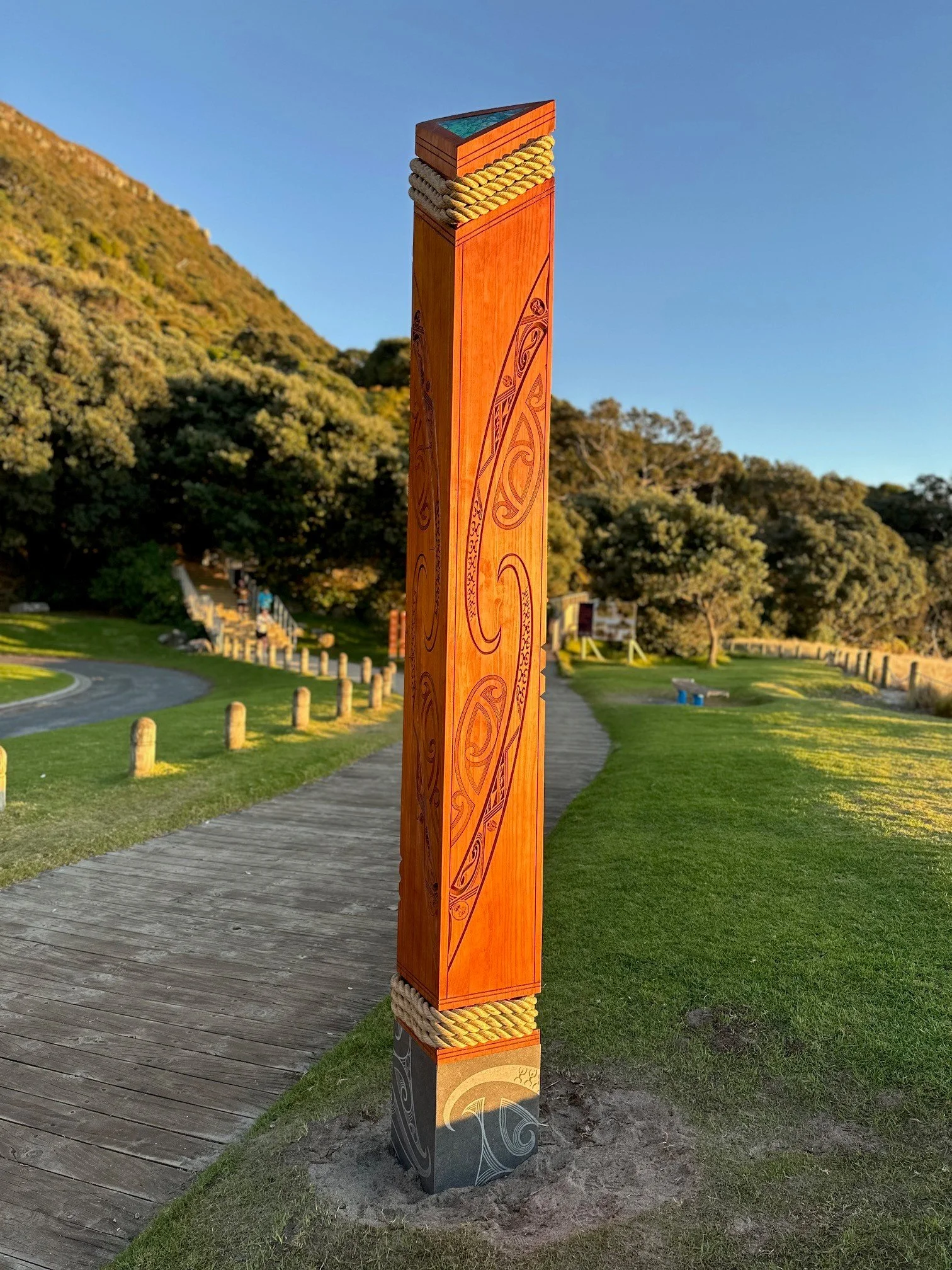 A tall wooden pole with traditional Maori carvings, wrapped with woven rope near the top, standing at the Mauao.