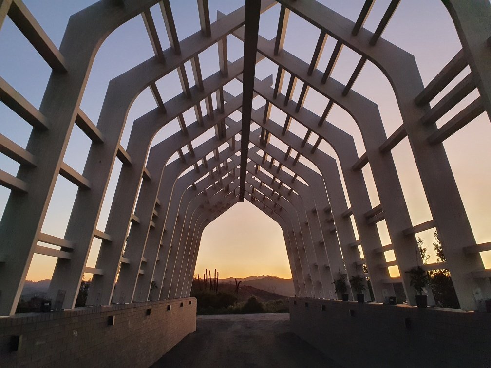Sunset view of Onemana Gateway, custom curved glulam portals and glulam purlins at a beachside retreat in New Zealand.