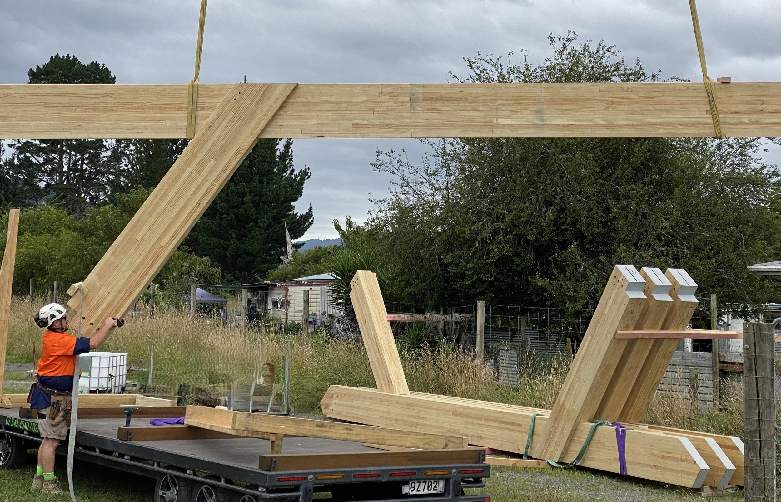 A person wearing safety gear unloading large glulam beams on a construction site.