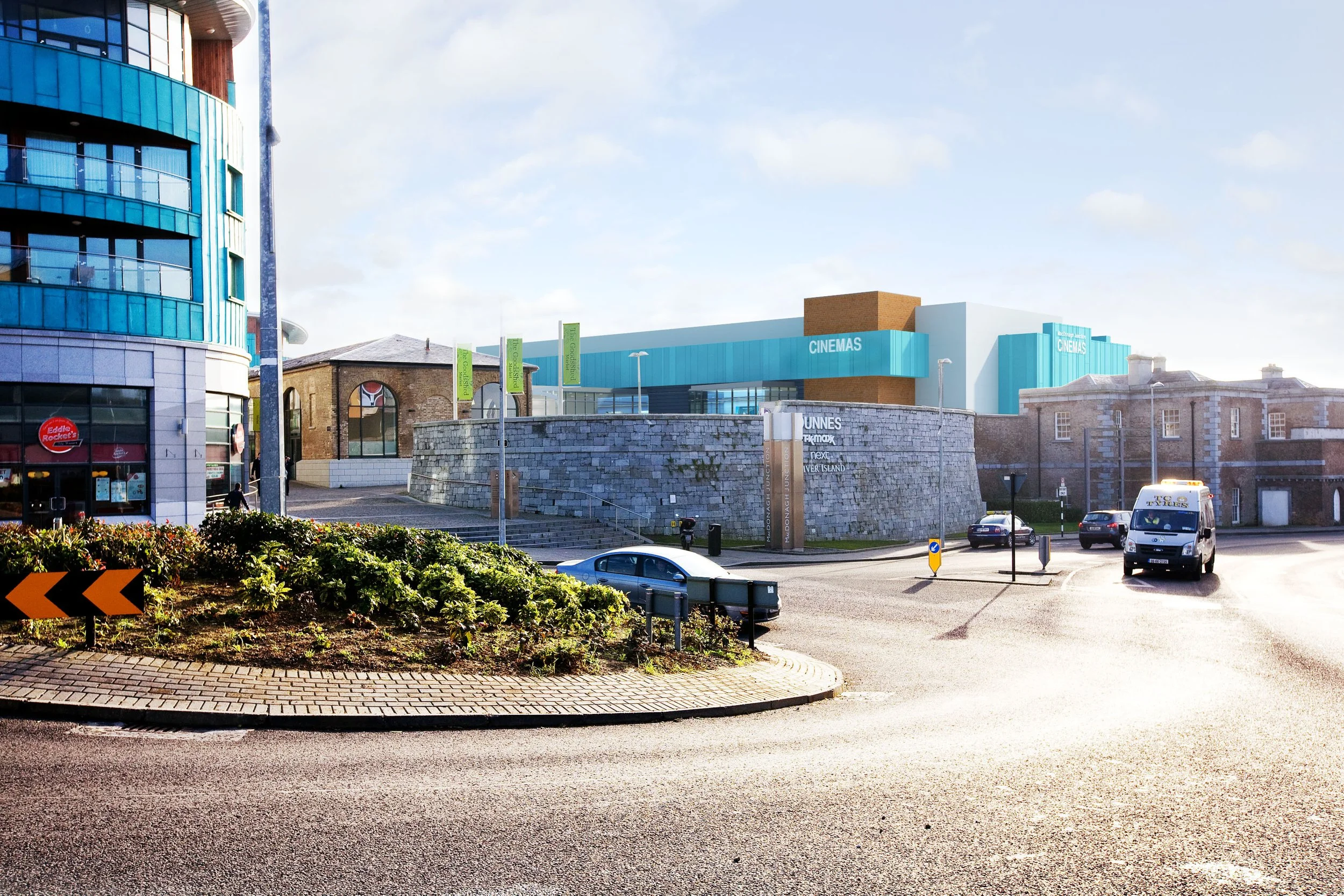 Cityscape with modern and historic buildings, a roundabout with cars, and a parking garage with a blue exterior in the background, under a clear sky.