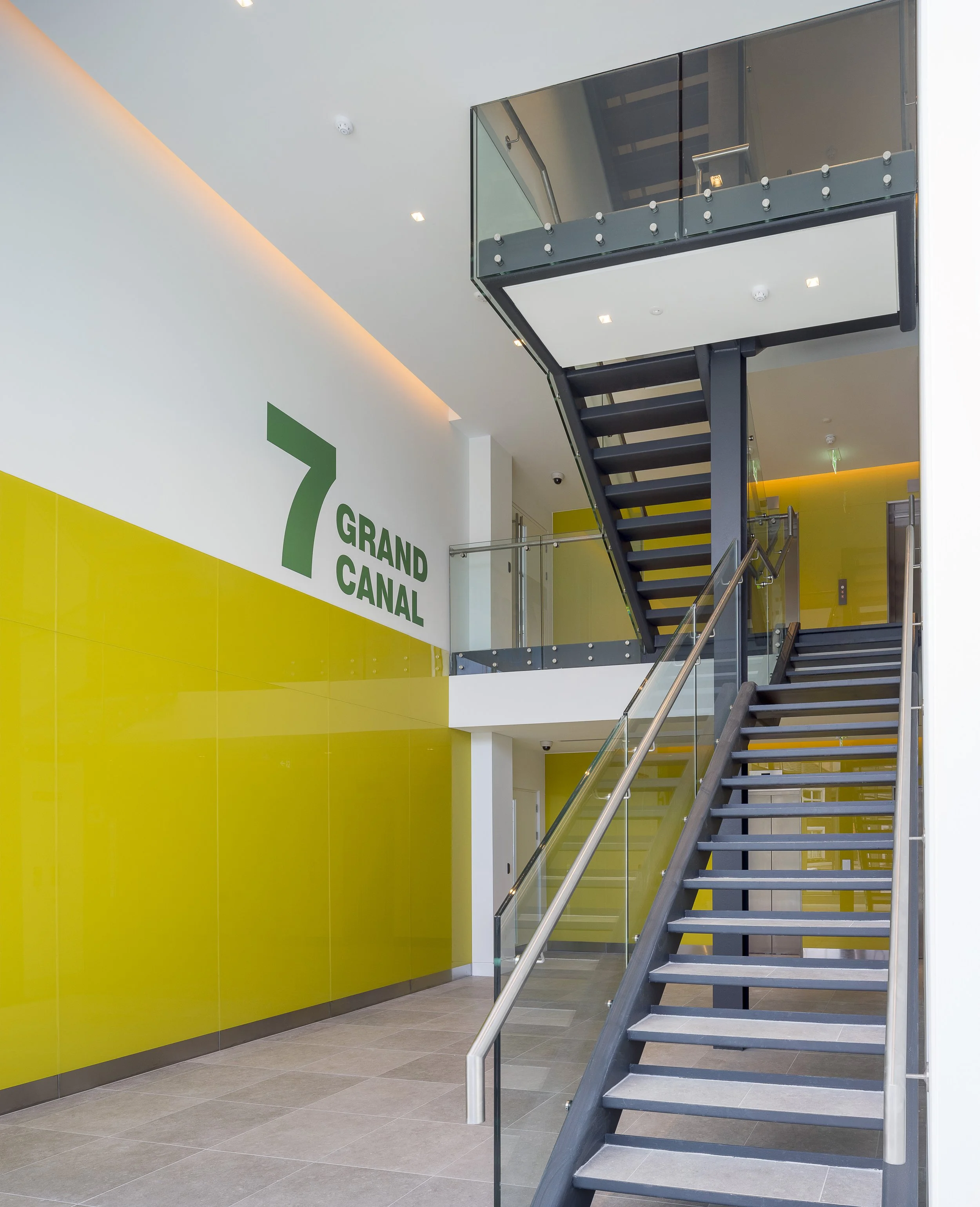 Interior of a modern building with a staircase, yellow wall panel, signage that reads '7 GRAND CANAL' on the wall.