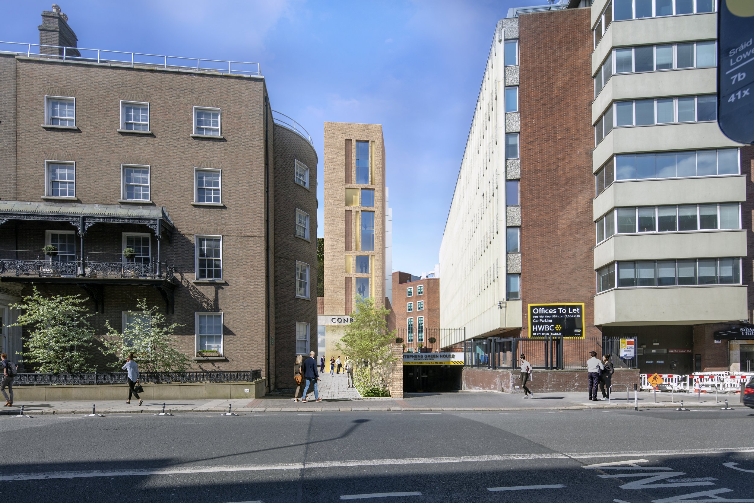 City street scene with tall buildings, pedestrians walking on sidewalk, trees, and a parking garage entrance in the background.