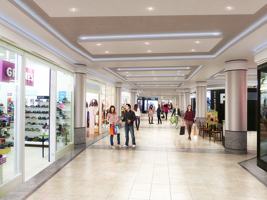 Interior view of a shopping mall corridor with several shoppers, stores, and seating areas.