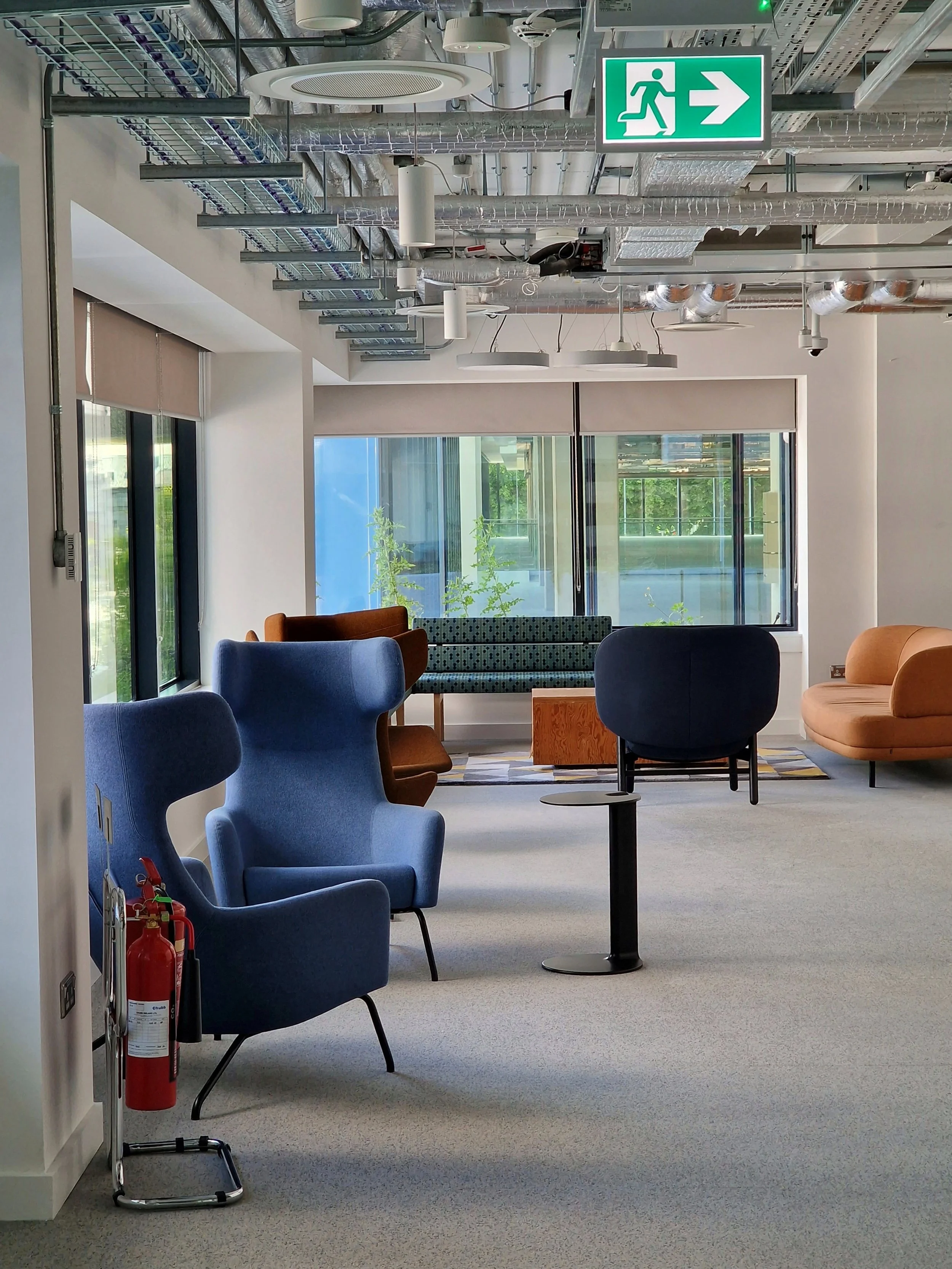 Modern office lounge area with colorful armchairs, sofas, and large windows bringing in natural light.