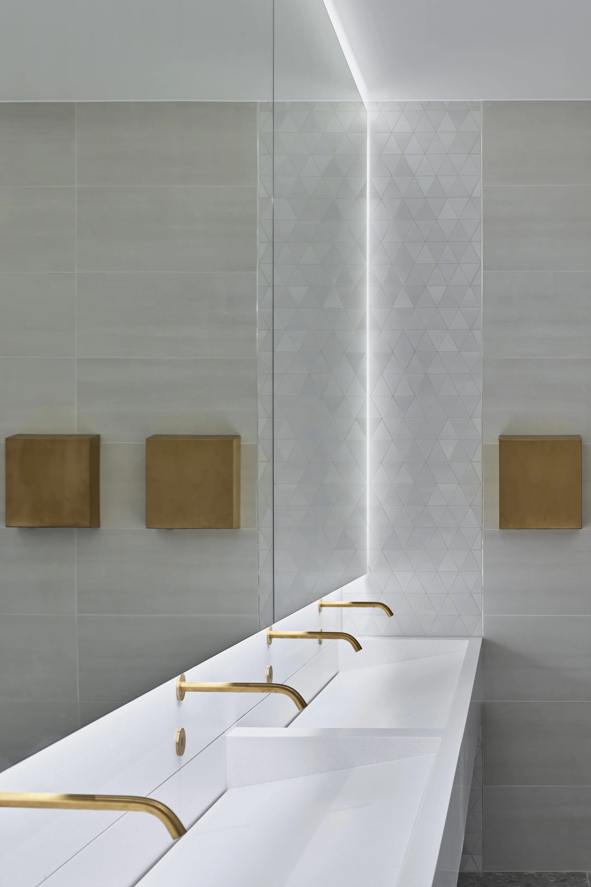 Modern bathroom with white countertop sinks, gold faucets, a large mirror, and beige wall-mounted storage cubbies.