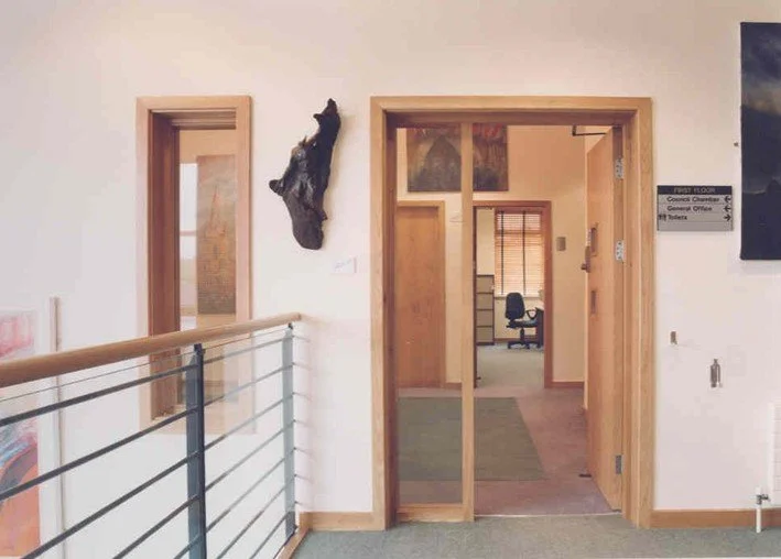 Interior view of an office building hallway with a doorway leading to a conference room, a chair visible, and a black decorative piece on the wall.