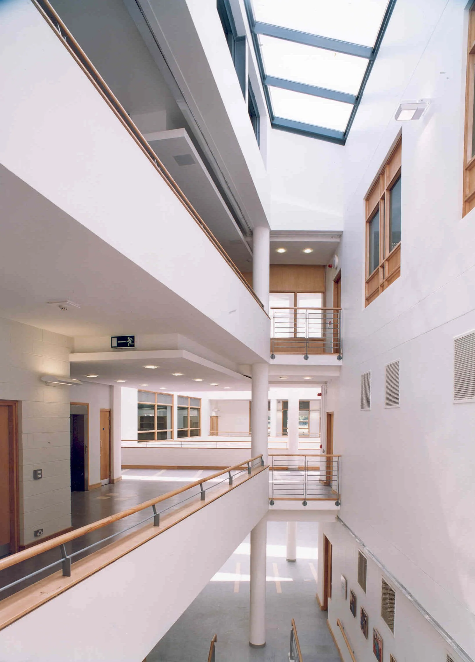 Interior view of a modern multi-story building with white walls, wooden accents, glass windows, and natural light streaming through skylights.