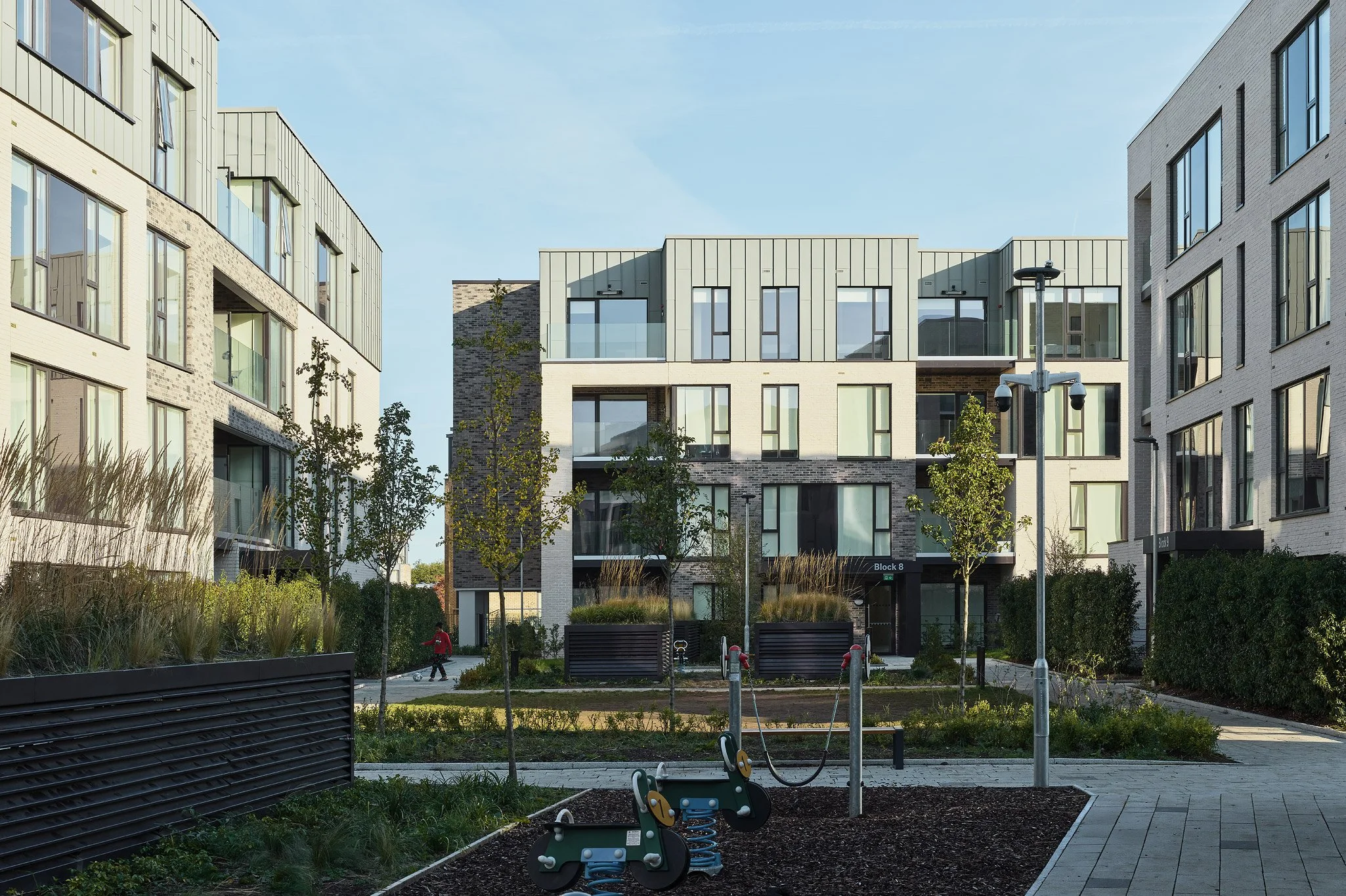 Modern apartment complex with landscaped courtyard, playground equipment, and a person walking.