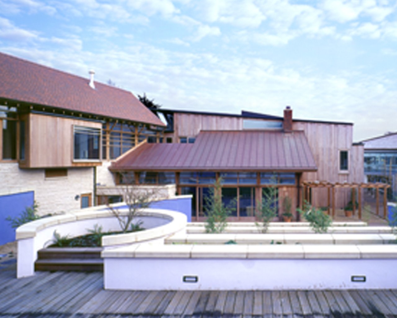 Modern house with wooden and stone exterior, a small garden, and a wooden deck under a partly cloudy sky.