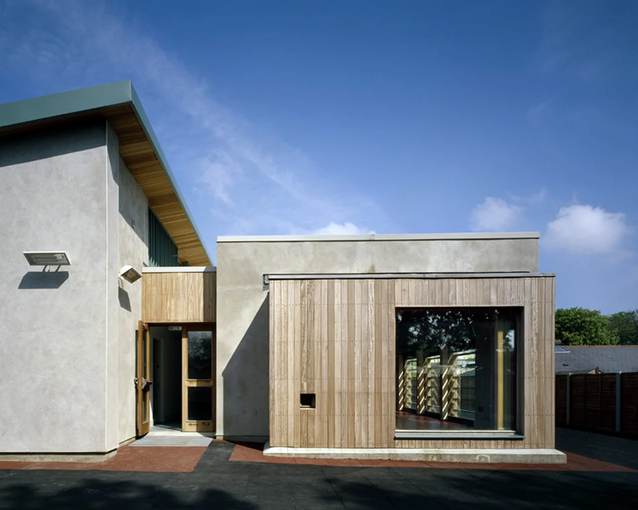 Modern house with a concrete and wooden exterior, large window, and blue sky in the background.