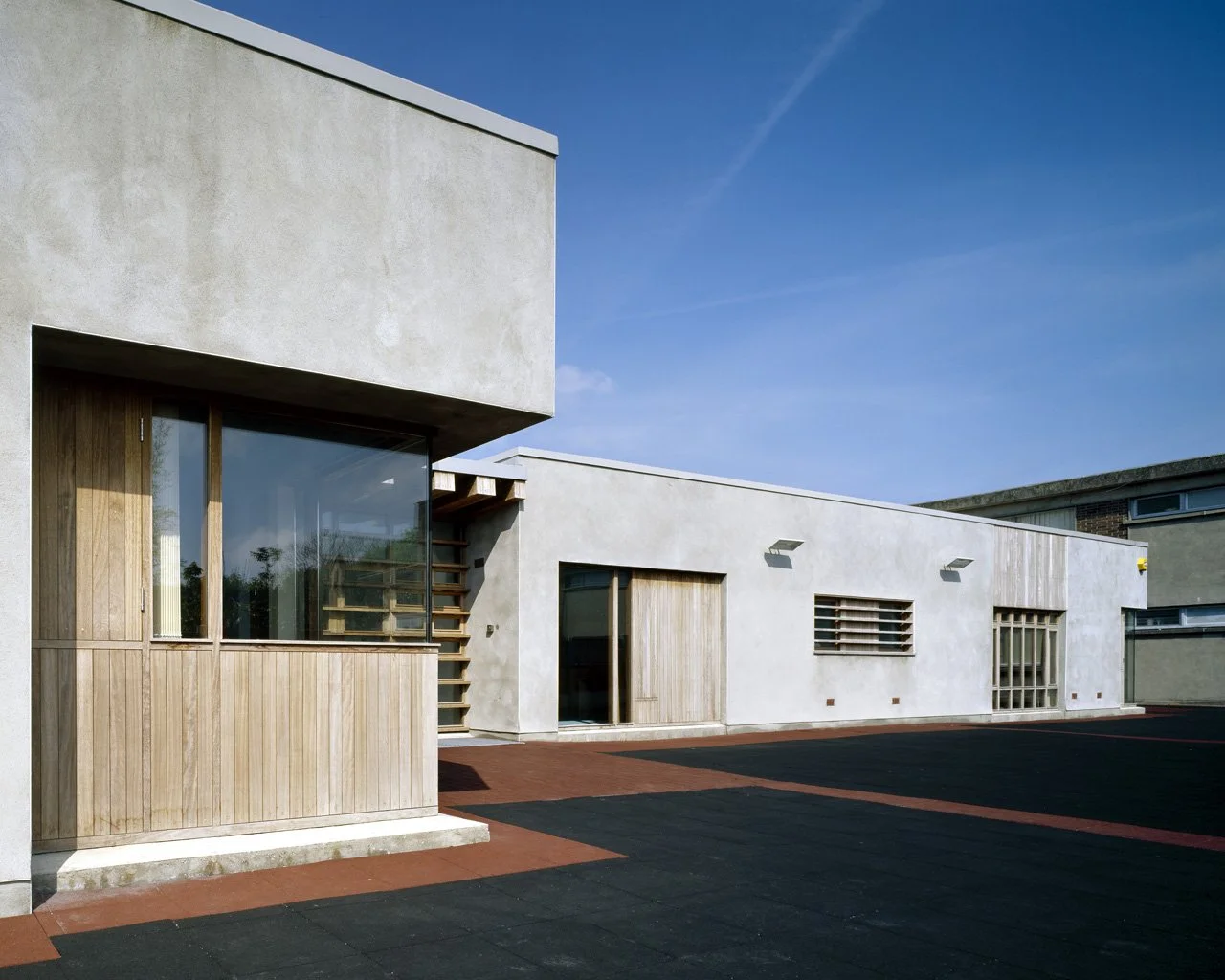 Modern building with white stucco walls, wooden accents, large windows, and concrete steps under a clear blue sky.