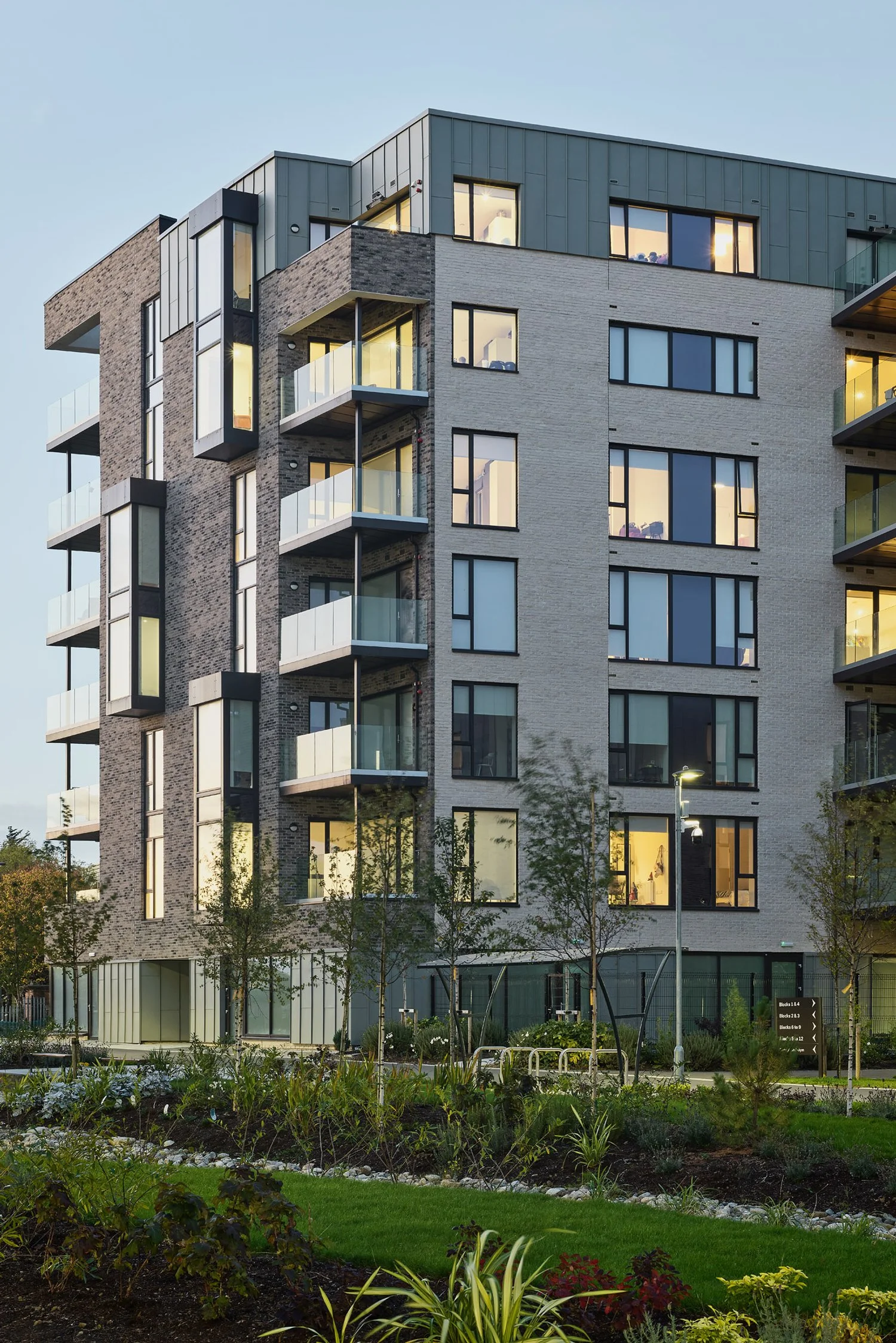 Modern multi-story apartment building with balconies and large windows surrounded by landscaped greenery.