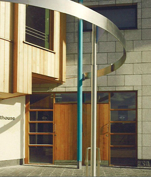 Modern building exterior with wooden and glass doors and a curved metal sculpture.