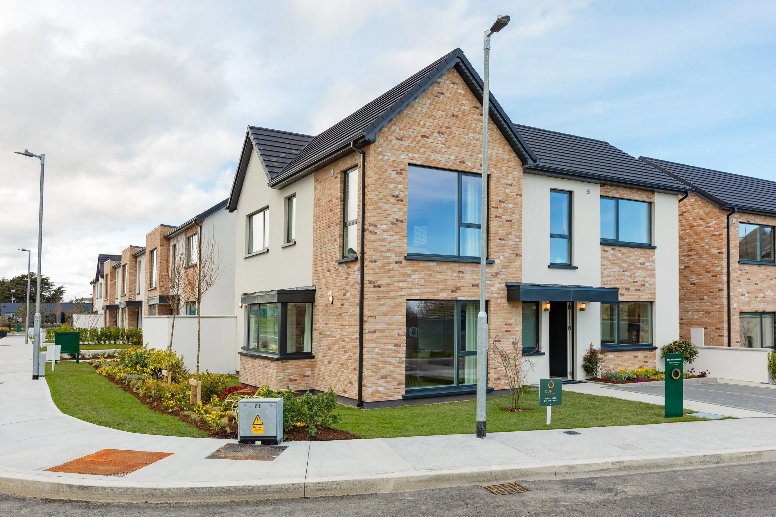 Modern residential townhouse with brick and white exterior, large windows, well-maintained lawn, and a sidewalk in a suburban neighborhood.