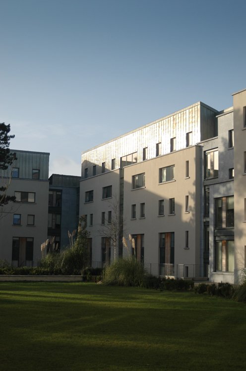 Modern apartment buildings with green lawn in foreground under a clear blue sky.