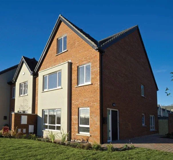Modern brick and stucco multi-story residential house with a steep gabled roof under a clear blue sky.