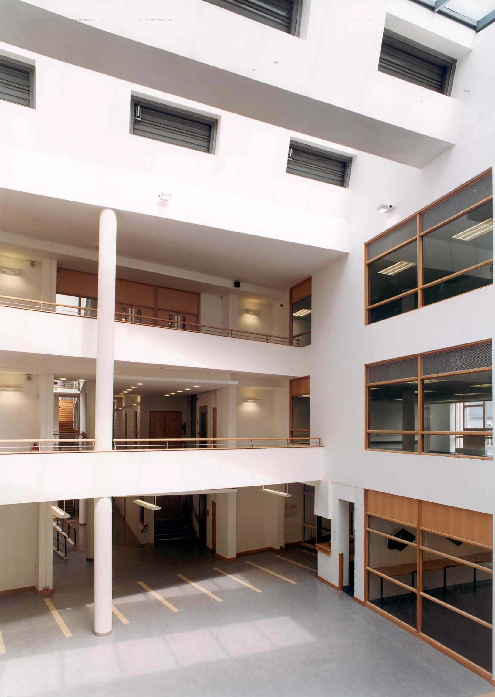 Interior view of a modern, multi-level office building atrium with white walls, wooden accents, large windows, and parking spaces on the ground floor.