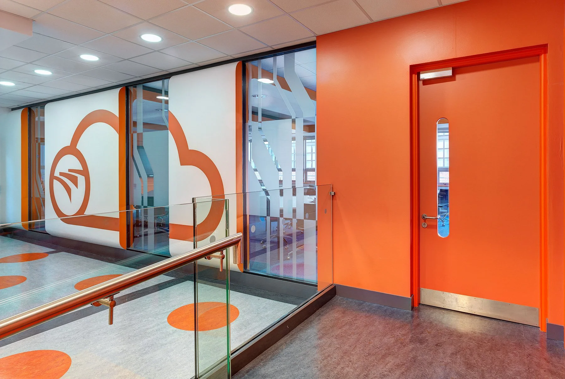 Interior of a modern building with orange and white walls, glass partition, and a door with a vertical window.