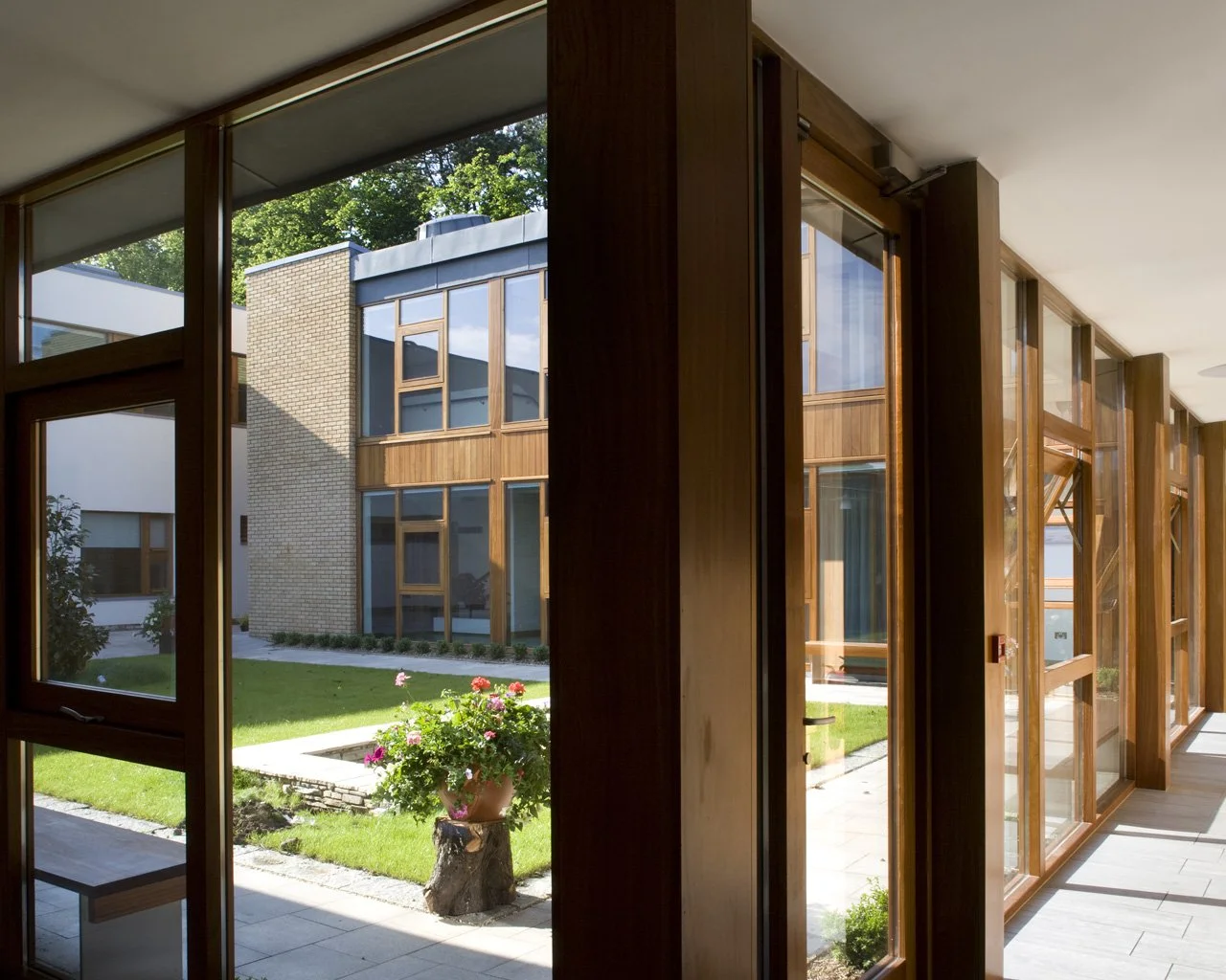 View of a modern building courtyard through large wooden framed glass windows inside a building.
