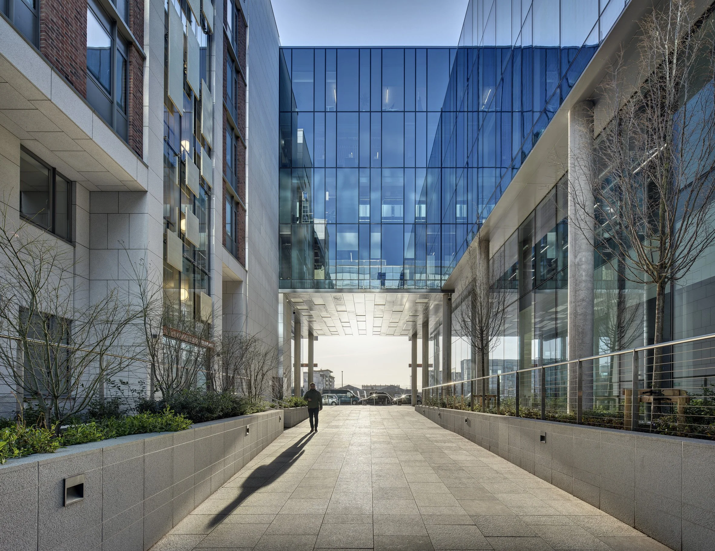Modern office building with glass facade, trees, and a person walking along a paved walkway.