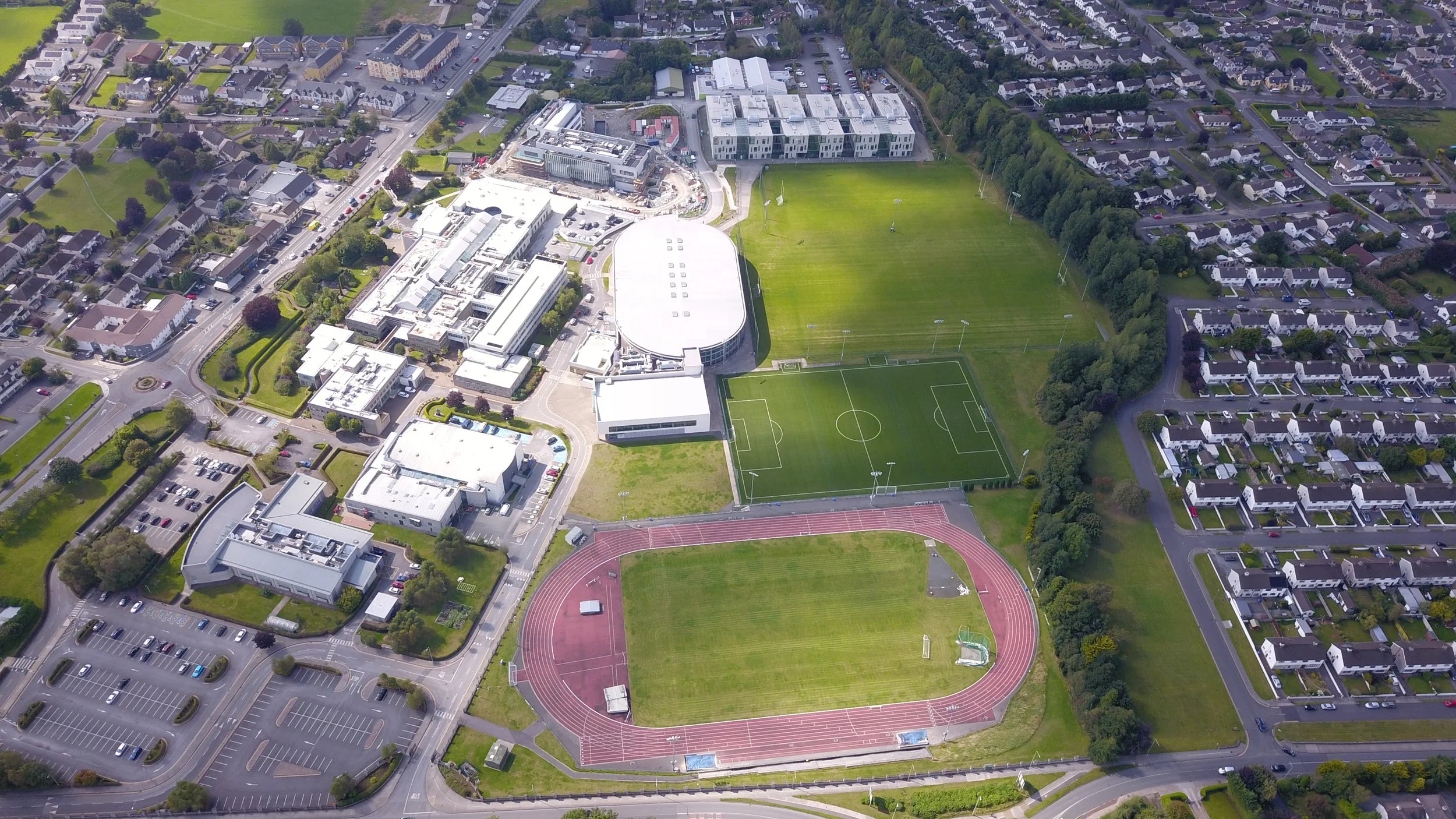 Aerial view of a school campus with sports fields, a running track, soccer fields, parking lots, and surrounding residential neighborhoods.
