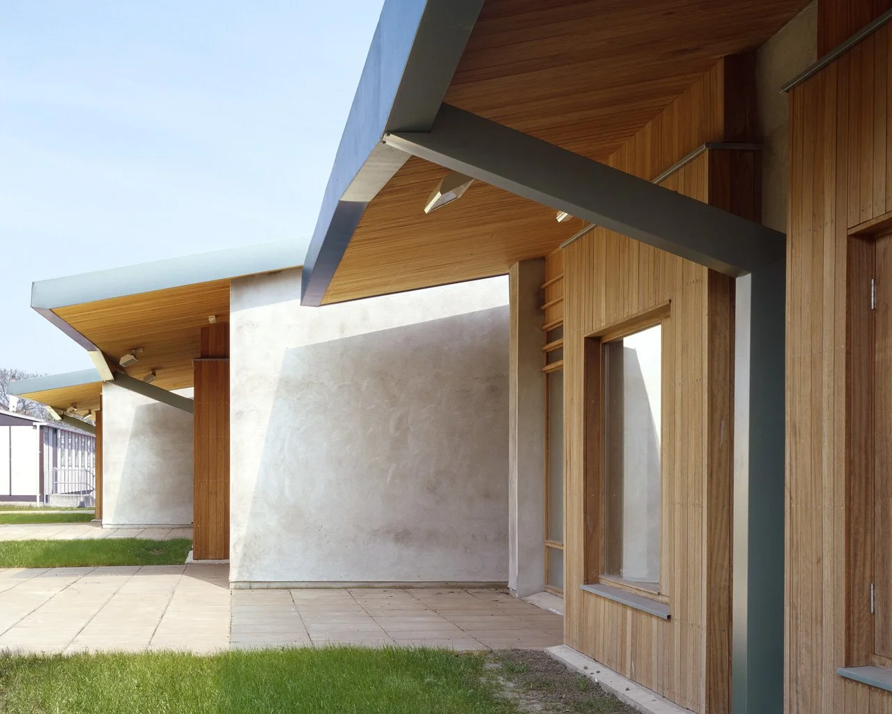 Modern building with wooden and concrete exterior, featuring slanted overhangs and large windows.