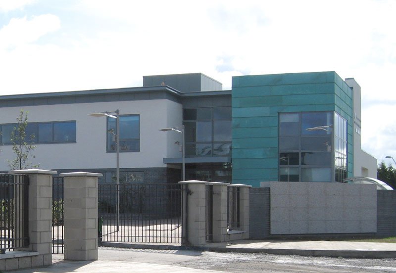 Modern commercial or institutional building with gray and teal exterior, gated entrance, and large windows.