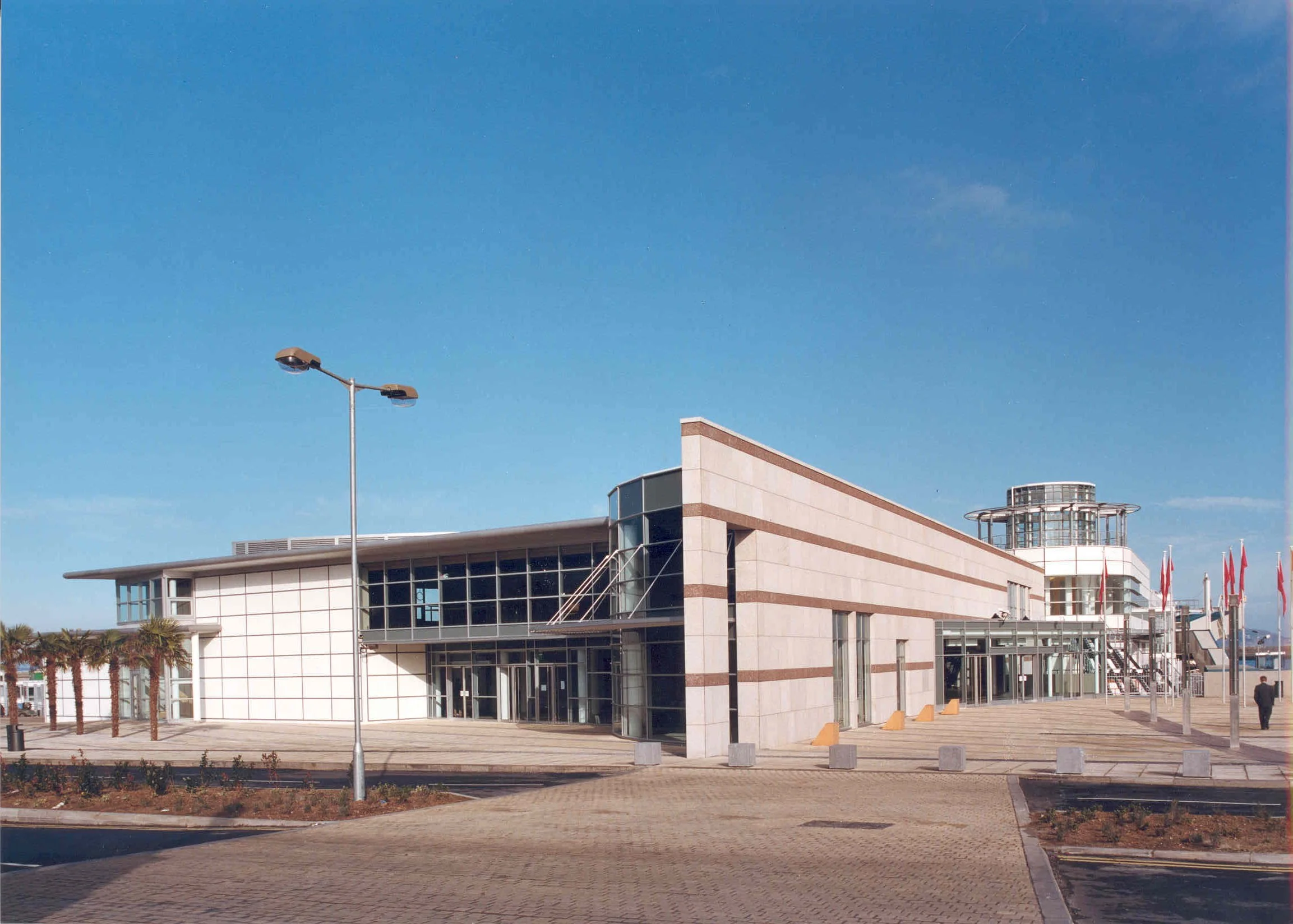 Modern building with glass windows, a tower, and flags in front, under a clear blue sky.
