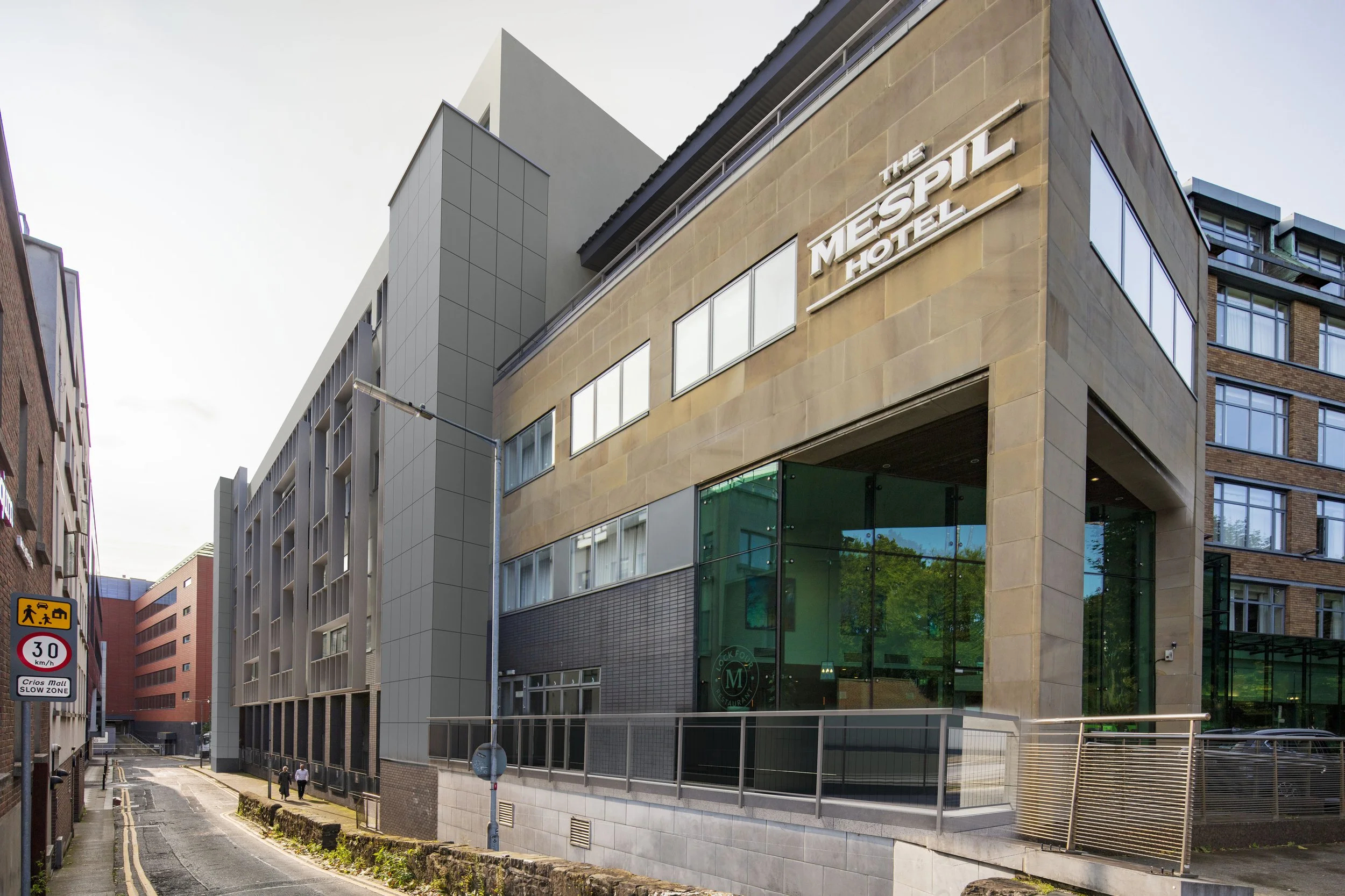 Modern hotel building named 'The Mespil Hotel' on a city street with pedestrians, glass windows, and nearby signage.