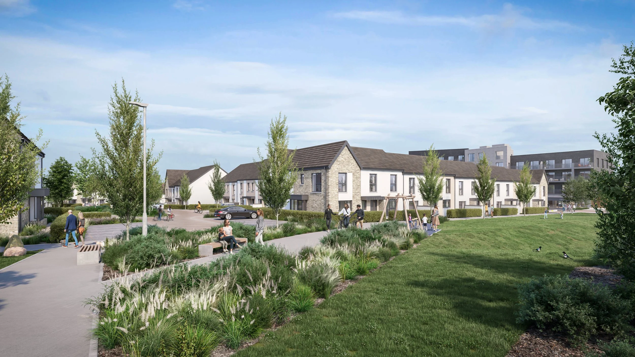 A modern residential complex with white townhouses and a large green park area with walking paths, trees, and children playing on the grass, during daytime with partly cloudy skies.