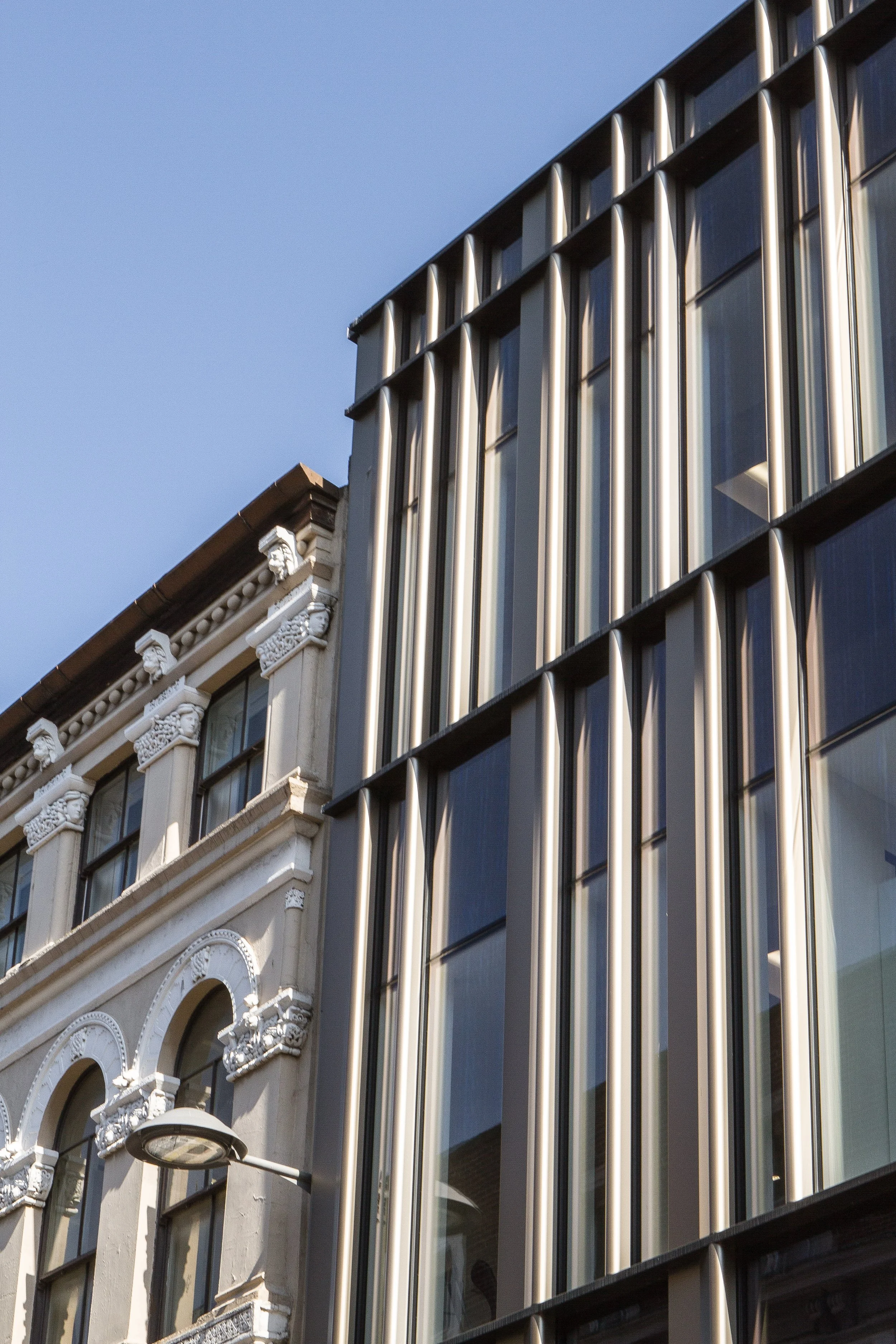 Close-up view of two adjacent buildings with contrasting architectural styles: an ornate, historic building with decorative details and an adjacent modern glass building with vertical metal panels.