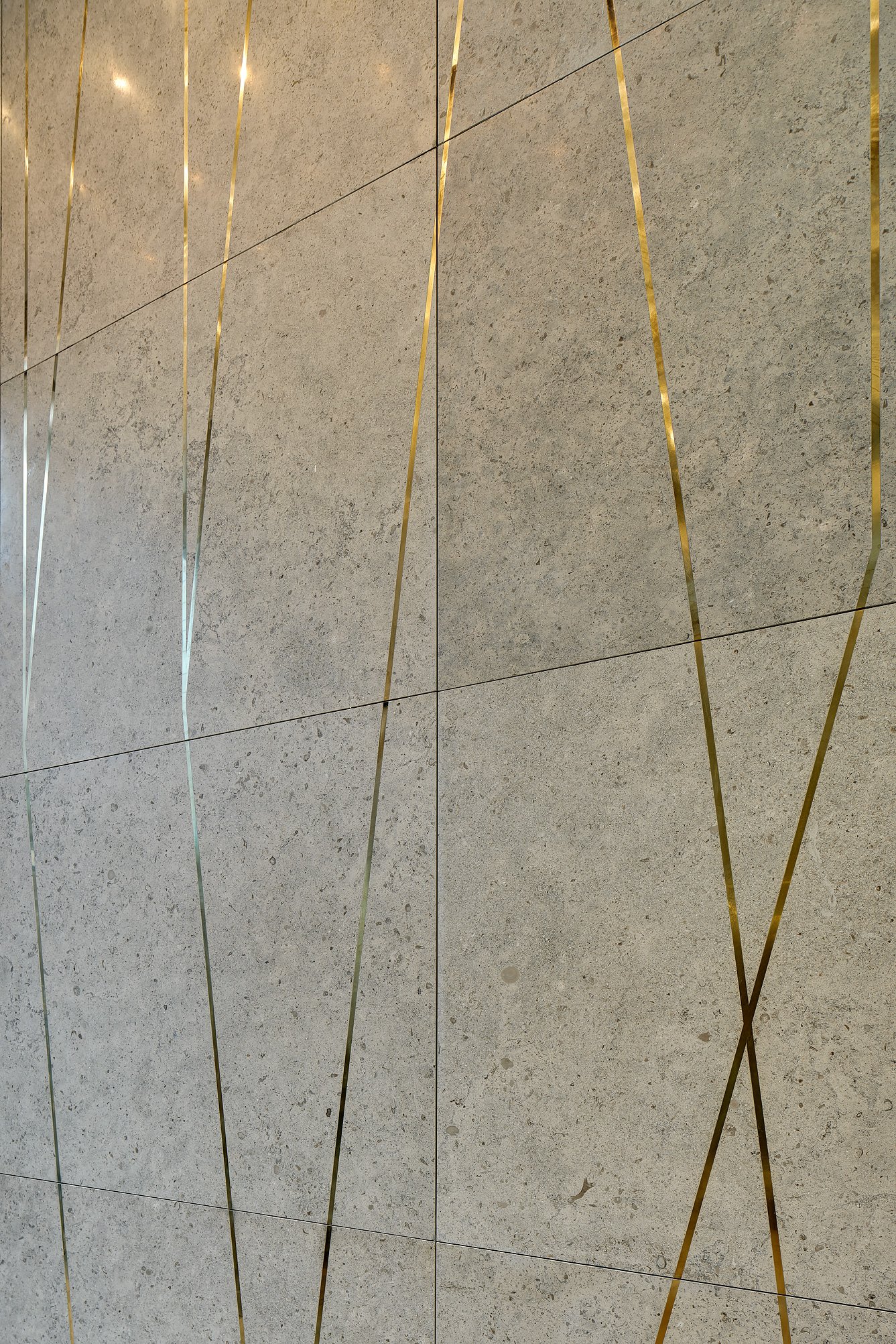 Close-up of a wall with beige textured stone tiles and decorative metallic gold lines intersecting vertically and diagonally.