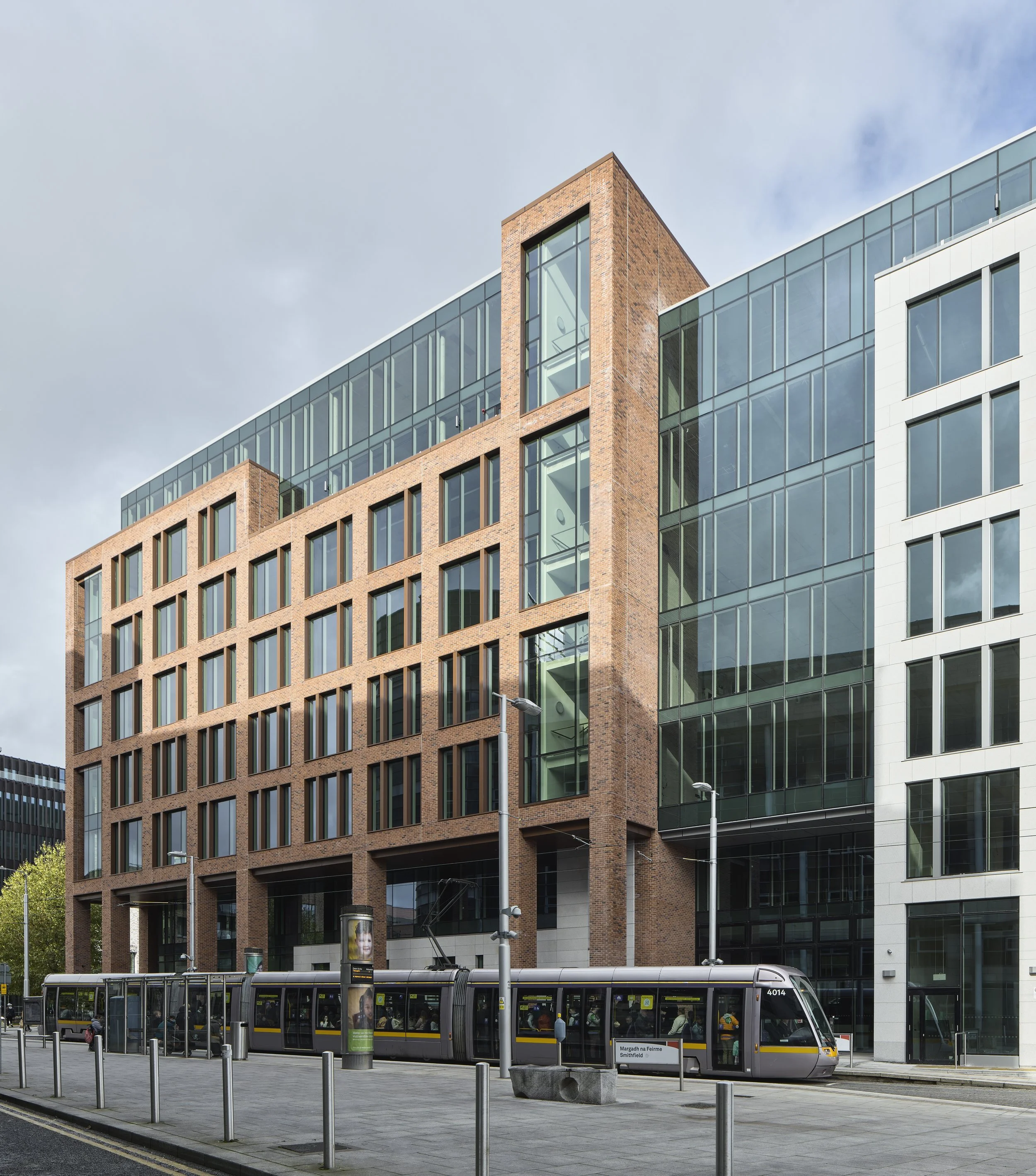 City street scene with modern multi-story glass and brick building, tram, street lamps, and sidewalk.