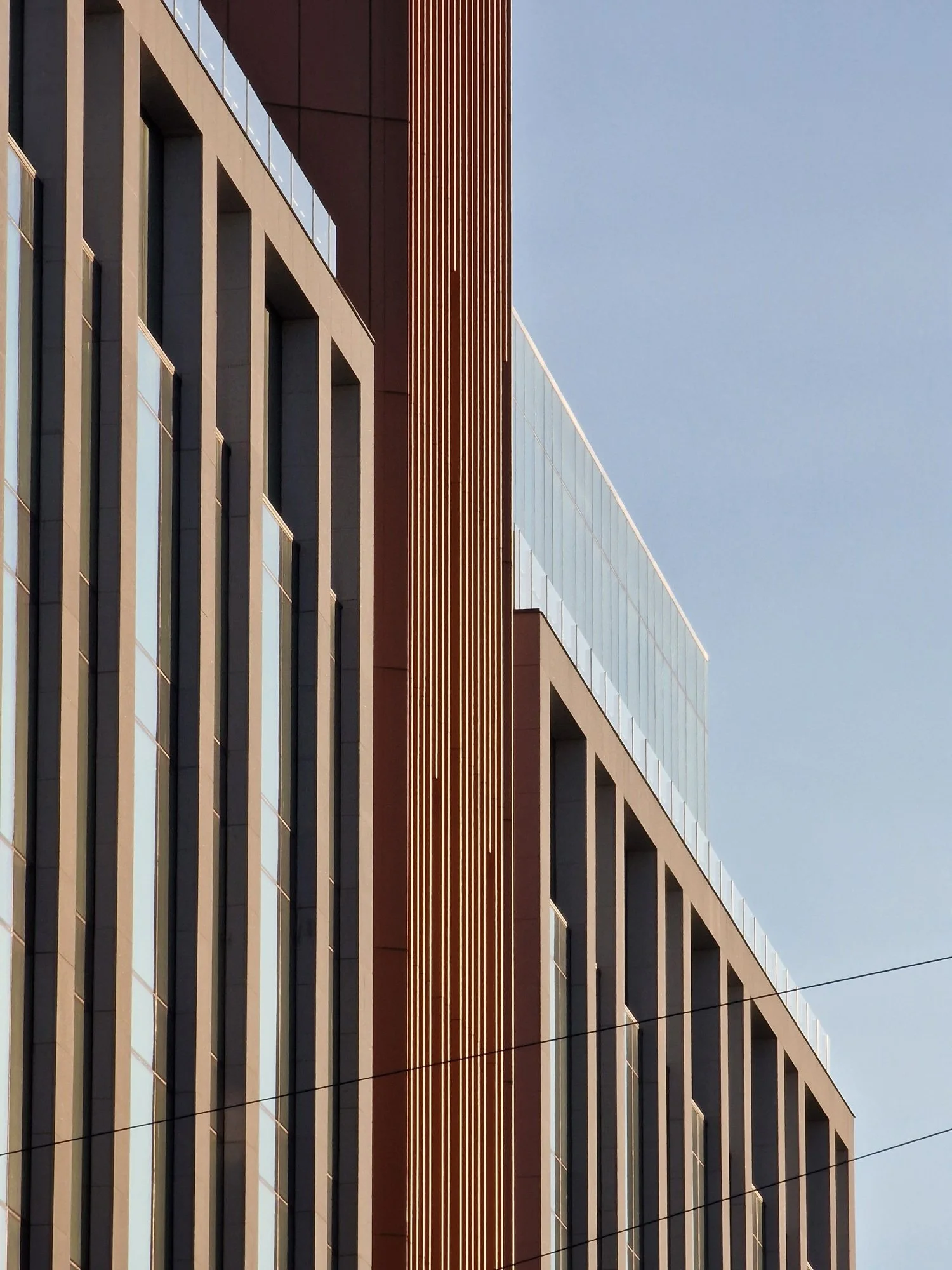 Modern building facade with vertical lines and glass windows, featuring geometric architectural design against a clear sky.