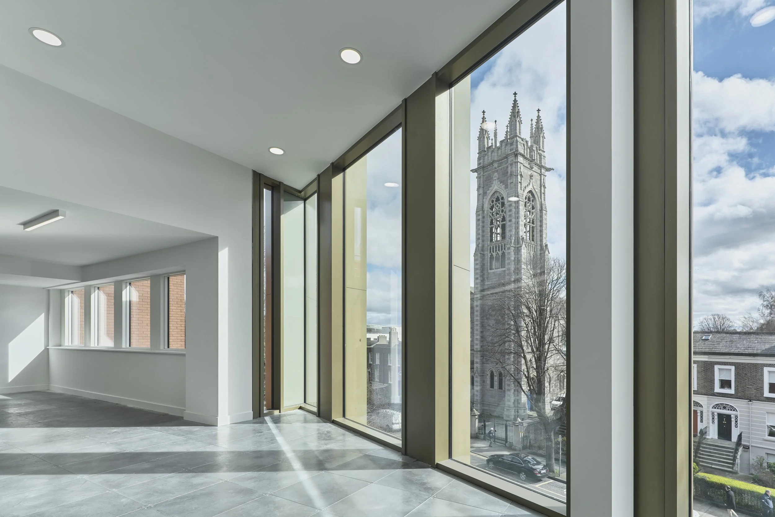 Empty modern room with floor-to-ceiling windows overlooking a historic church tower and street view.